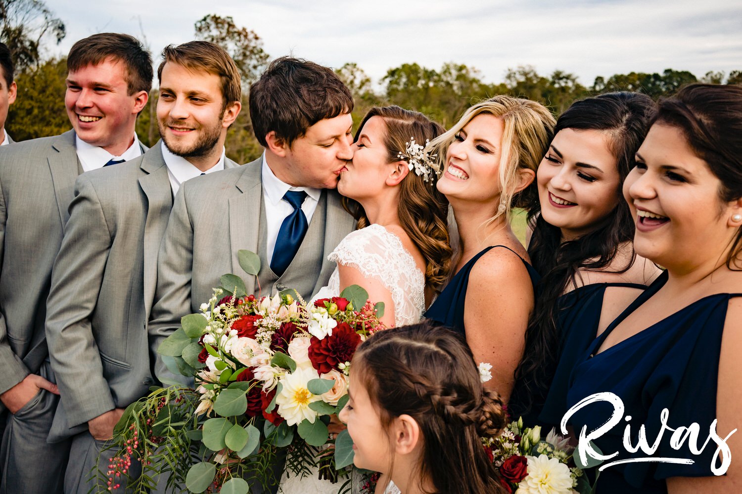 A colorful, close-up picture of a bride and groom sharing a kiss as they're surrounded by their wedding party on their fall wedding day in Virginia. 