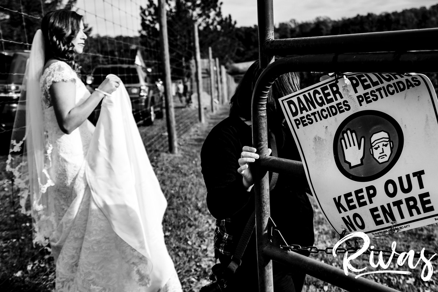 A candid black and white picture of a woman holding a gate open so a bride can enter a vineyard on her wedding afternoon at Hamilton Station Vineyard in Virginia. 