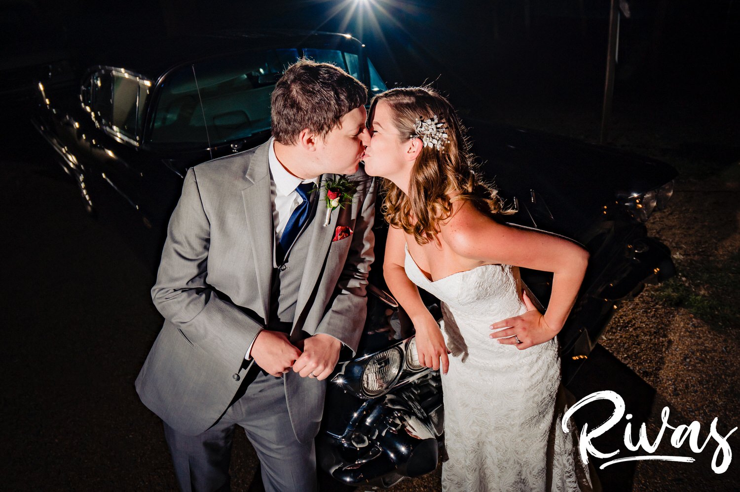 A colorful, candid picture of a bride and groom sharing a kiss as they lean up against a classic car at the end of their fall wedding day at The Barns at Hamilton Station Vineyard. 