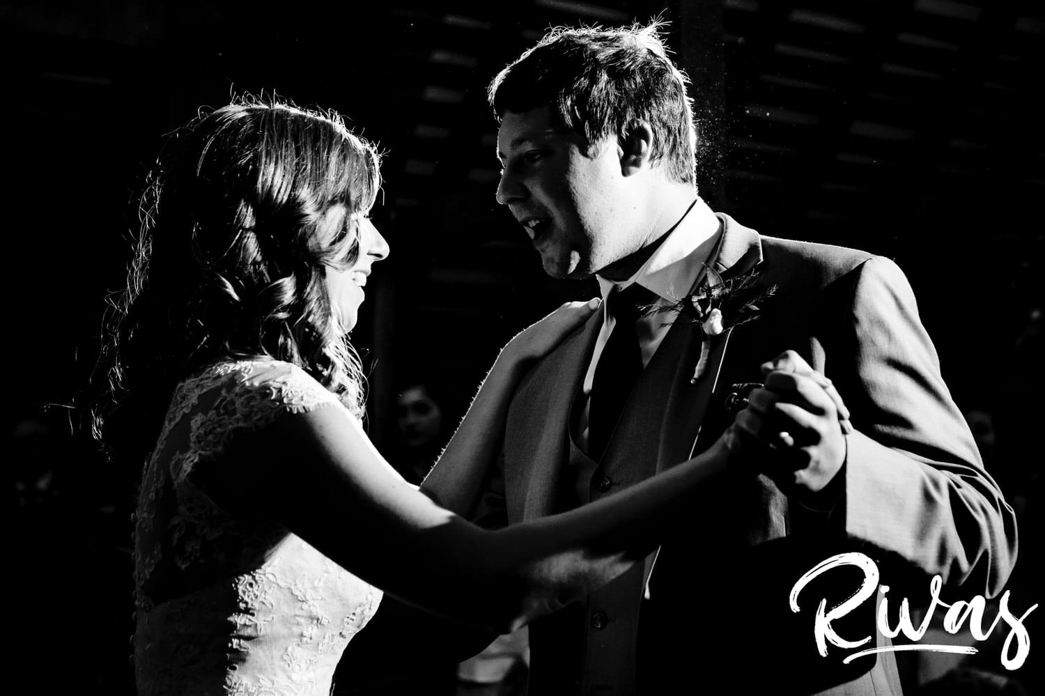 A candid black and white picture of a bride and groom laughing together as they share their first dance during their fall wedding reception. 