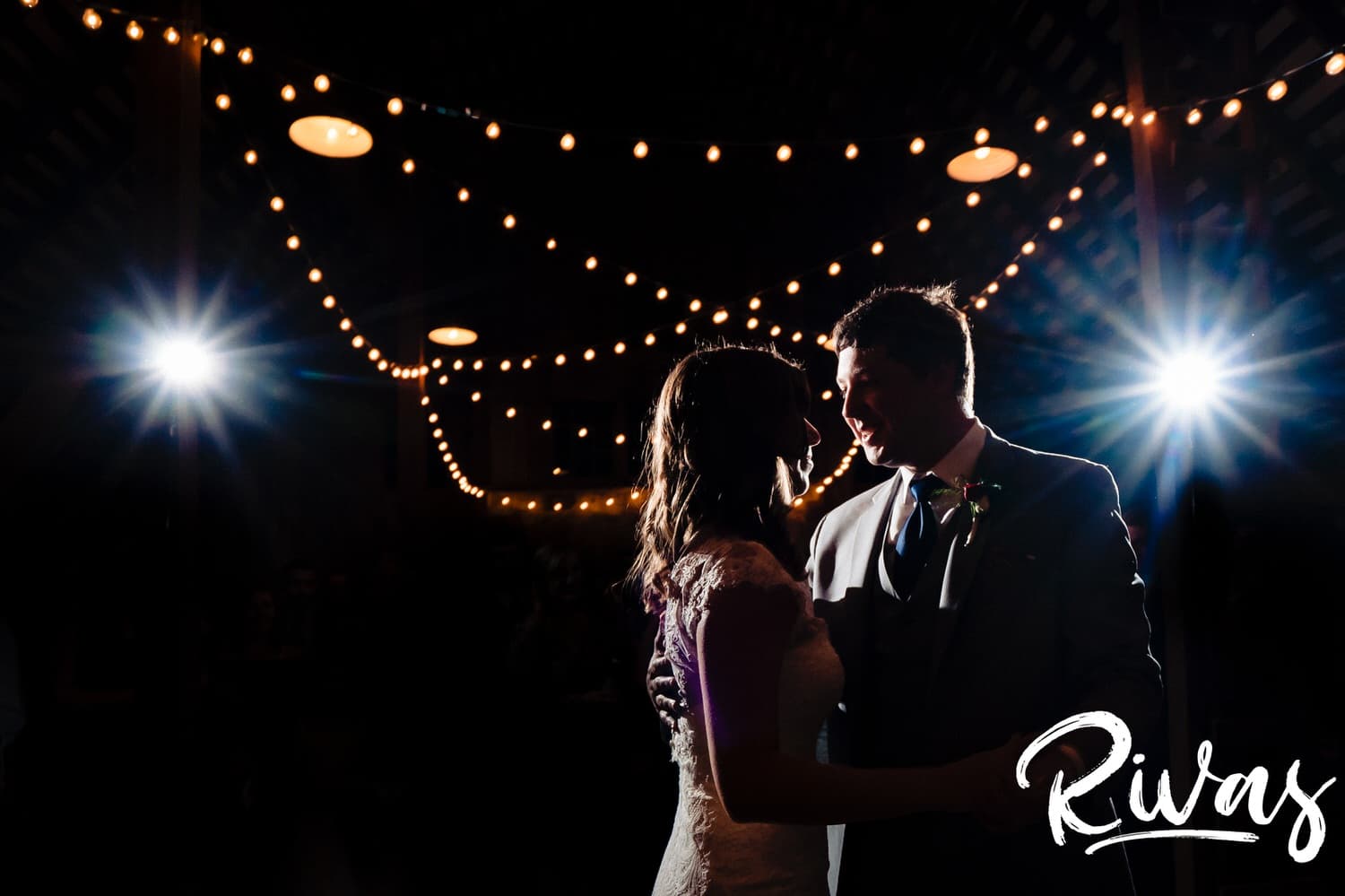A close-up, colorful picture of a bride and groom against a background of twinkly lights sharing their first dance on the day of their fall wedding. 