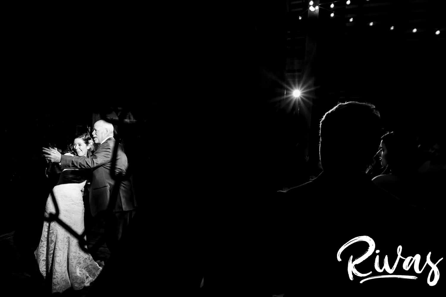 A candid black and white picture taken from somewhere in the crowd of a bride and her dad dancing and pointing at something during her fall wedding reception at The Barns at Hamilton Station Vineyards. 