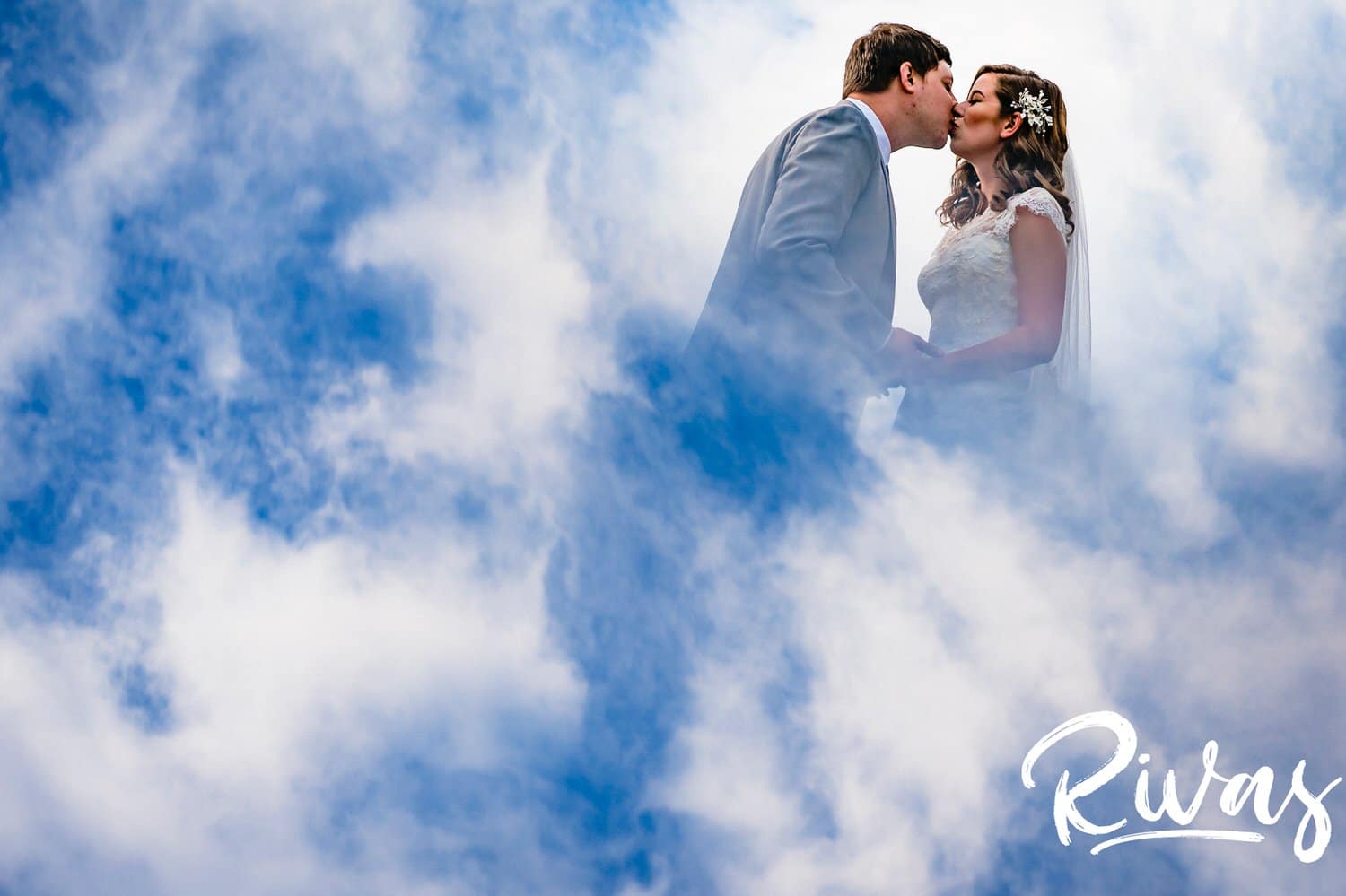 A colorful, abstract picture of a bride and groom sharing a kiss completely surrounded by blue sky and clouds on their fall wedding day at The Barns at Hamilton Station Vineyard. 