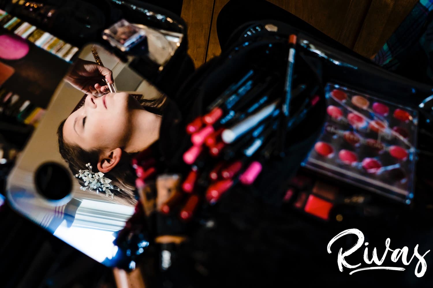 A colorful picture of a bride getting her makeup done, reflected in the mirror of a makeup compact sitting on a table on the afternoon of her fall wedding at The Barns at Hamilton Station Vineyard. 