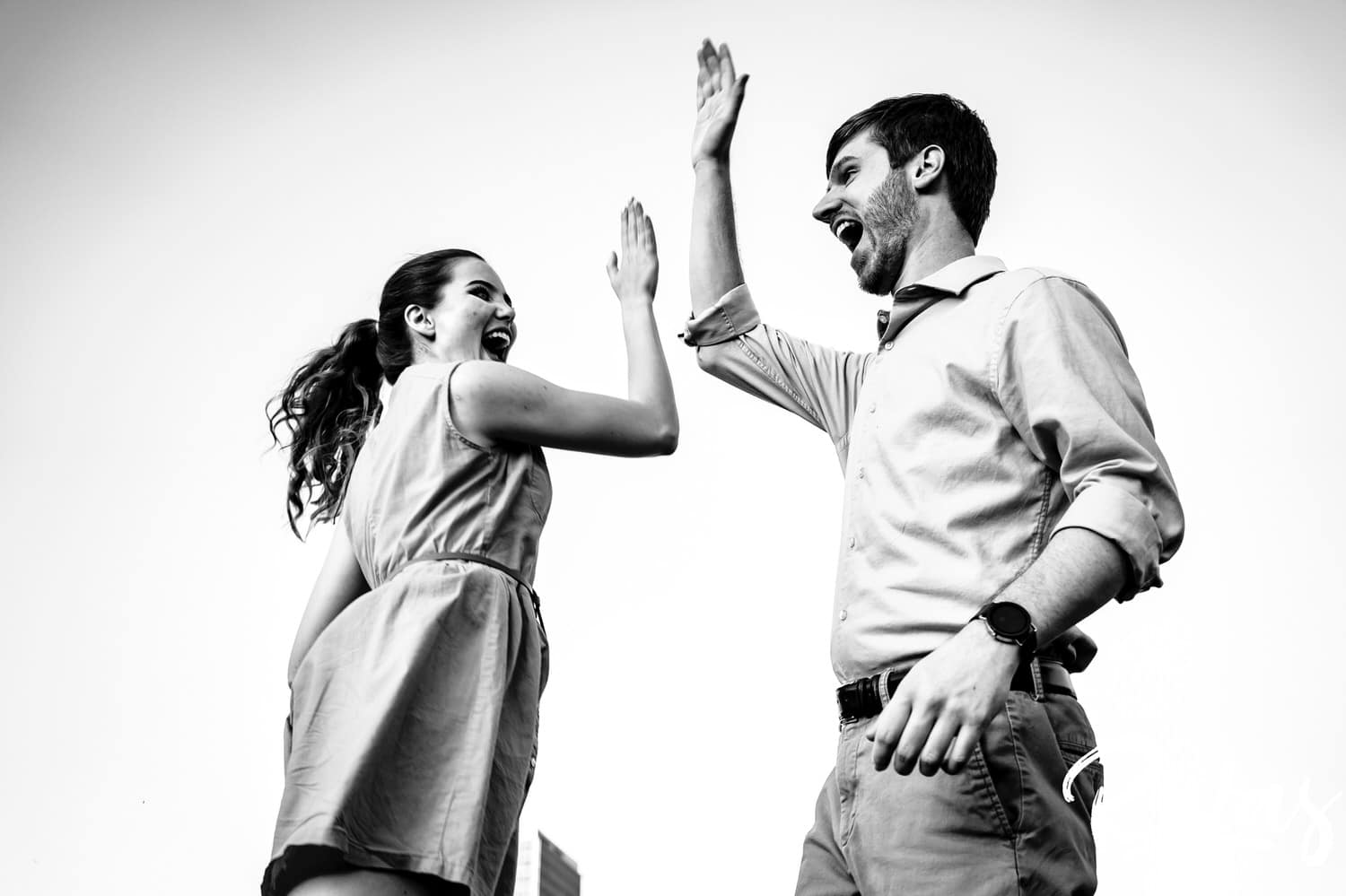 A playful black and white picture of an engaged couple high-fiving each other at the end of their summer engagement session. 