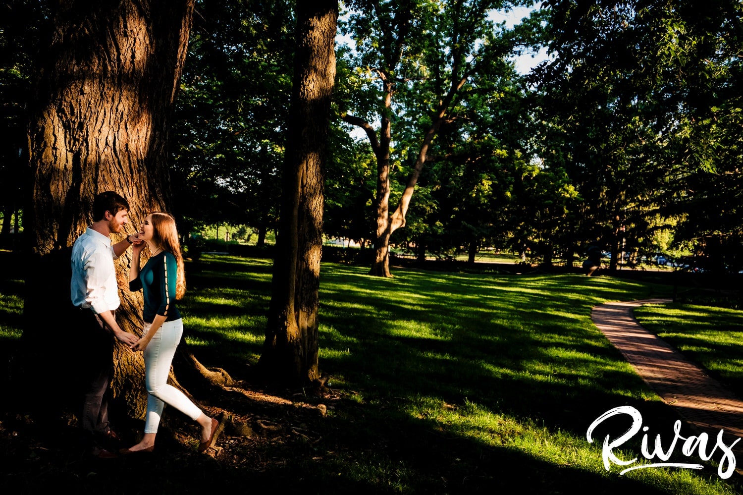 A colorful picture of an engaged couple standing underneath a tree in a splash of sunlight on the grounds of The Nelson during their summer engagement session. 