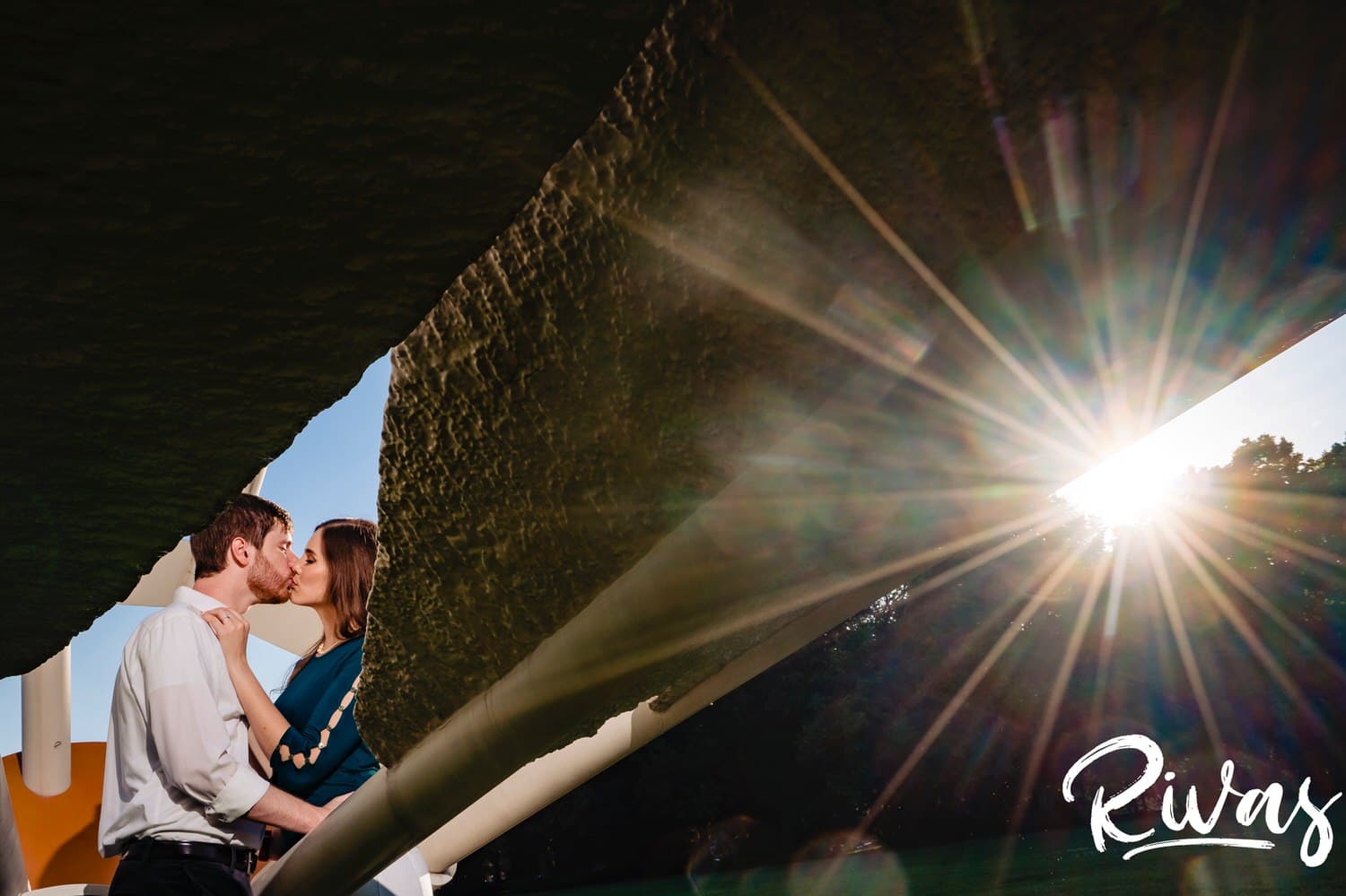 A vibrant portrait of an engaged couple in the center of a shuttlecock sharing a kiss during their summer engagement session at The Nelson in Kansas City. 