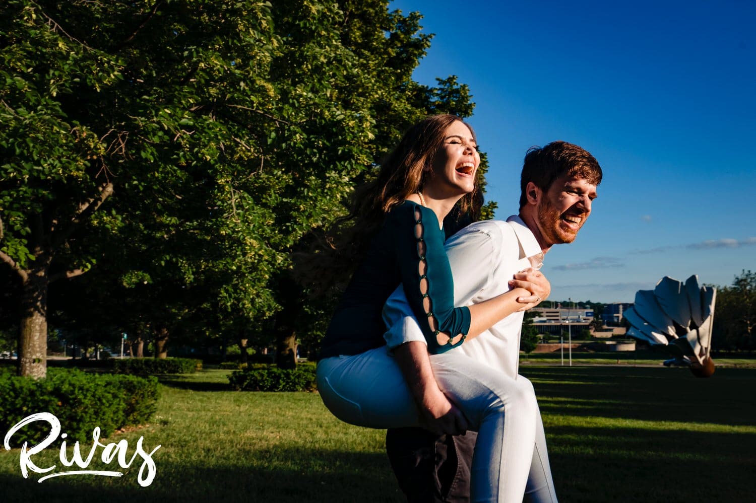 A colorful, candid picture of a man carrying his fiance piggyback during their summer engagement session in Kansas City. 