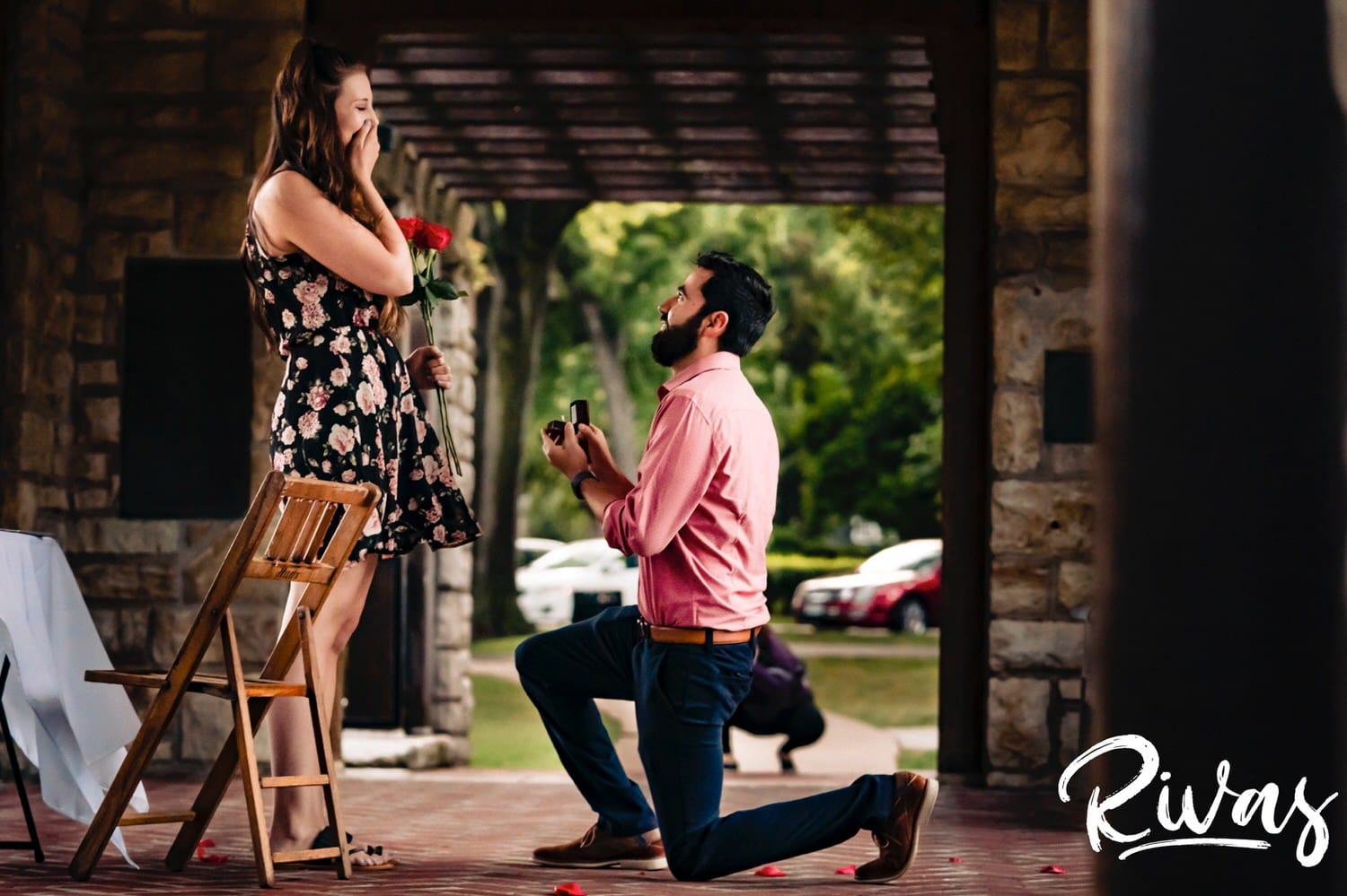 A colorful, candid picture of a man down on one knee holding a ring box and surprise proposing to his girlfriend at Loose Park in Kansas City. 