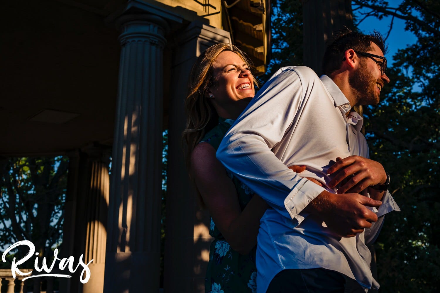 A vibrant, playful picture of a woman sneaking up on and tickling her fiance during their summer engagement session with their wedding photographer. 
