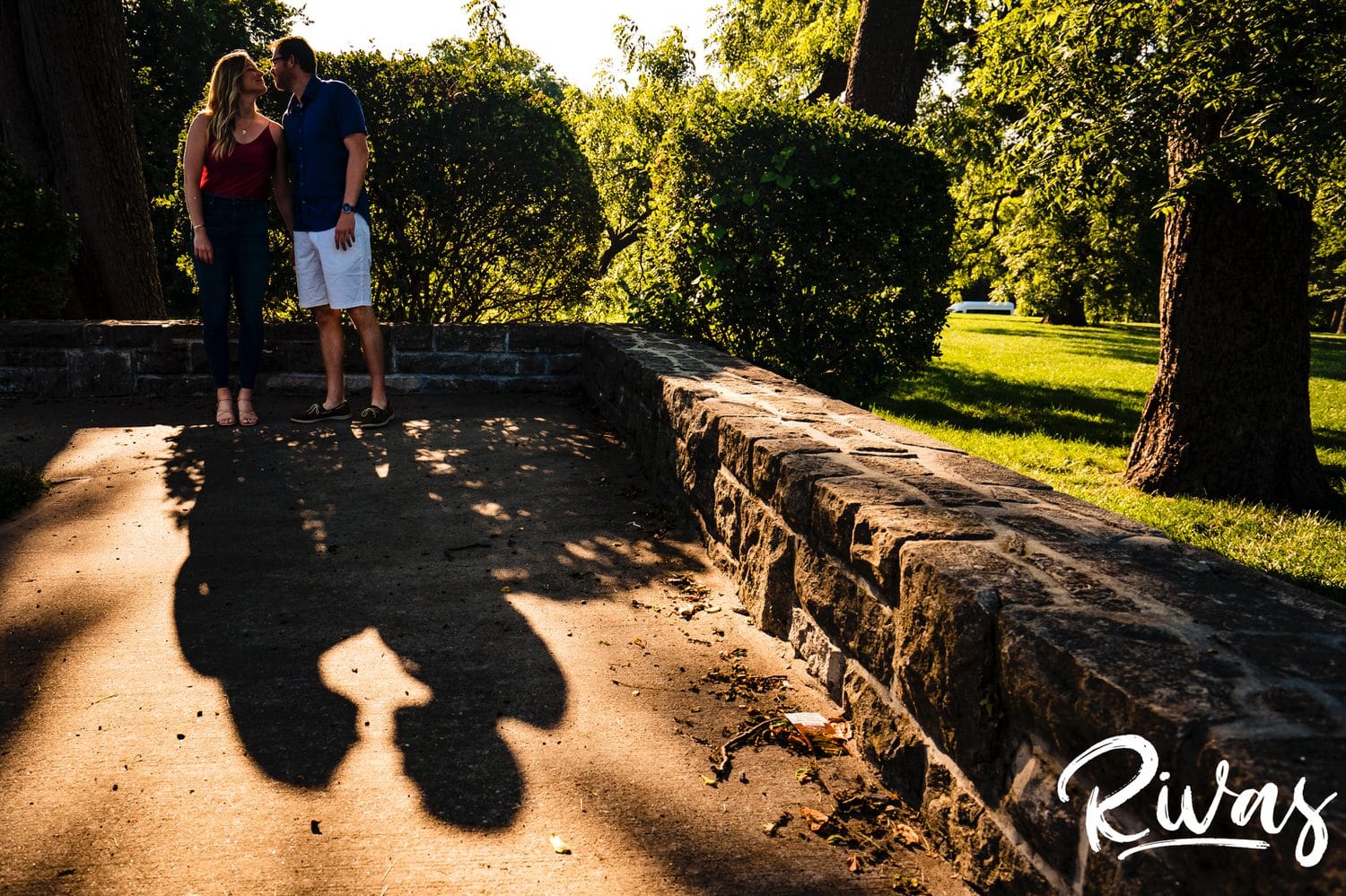 A colorful portrait of an engaged couple sharing a kiss, their shadows visible on the sidewalk in front of them during a summer engagement session with their wedding photographer in Kansas City. 