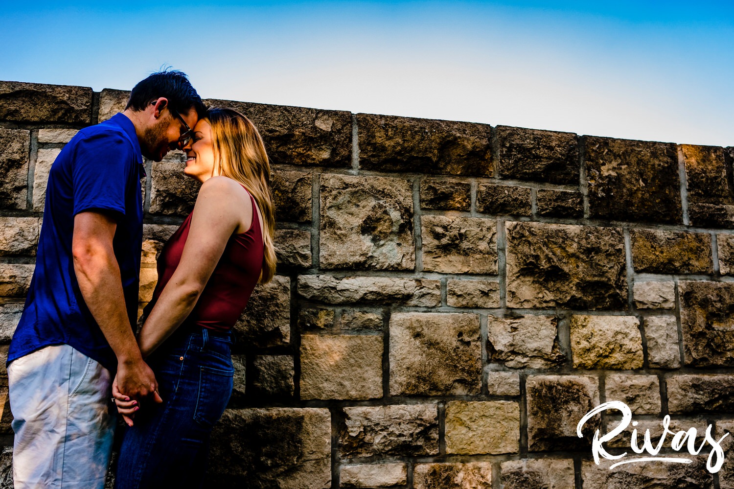 A colorful picture of an engaged couple leaning up against a stone wall during their summer engagement session with their wedding photographer at Kansas City's Loose Park. 