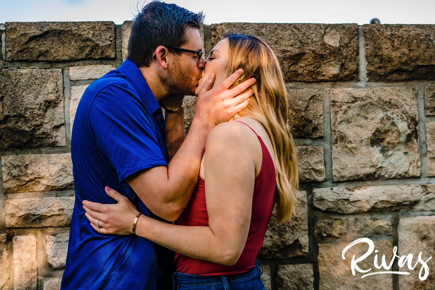 A colorful picture of an engaged couple leaning up against a stone wall during their summer engagement session with their wedding photographer at Kansas City's Loose Park. 