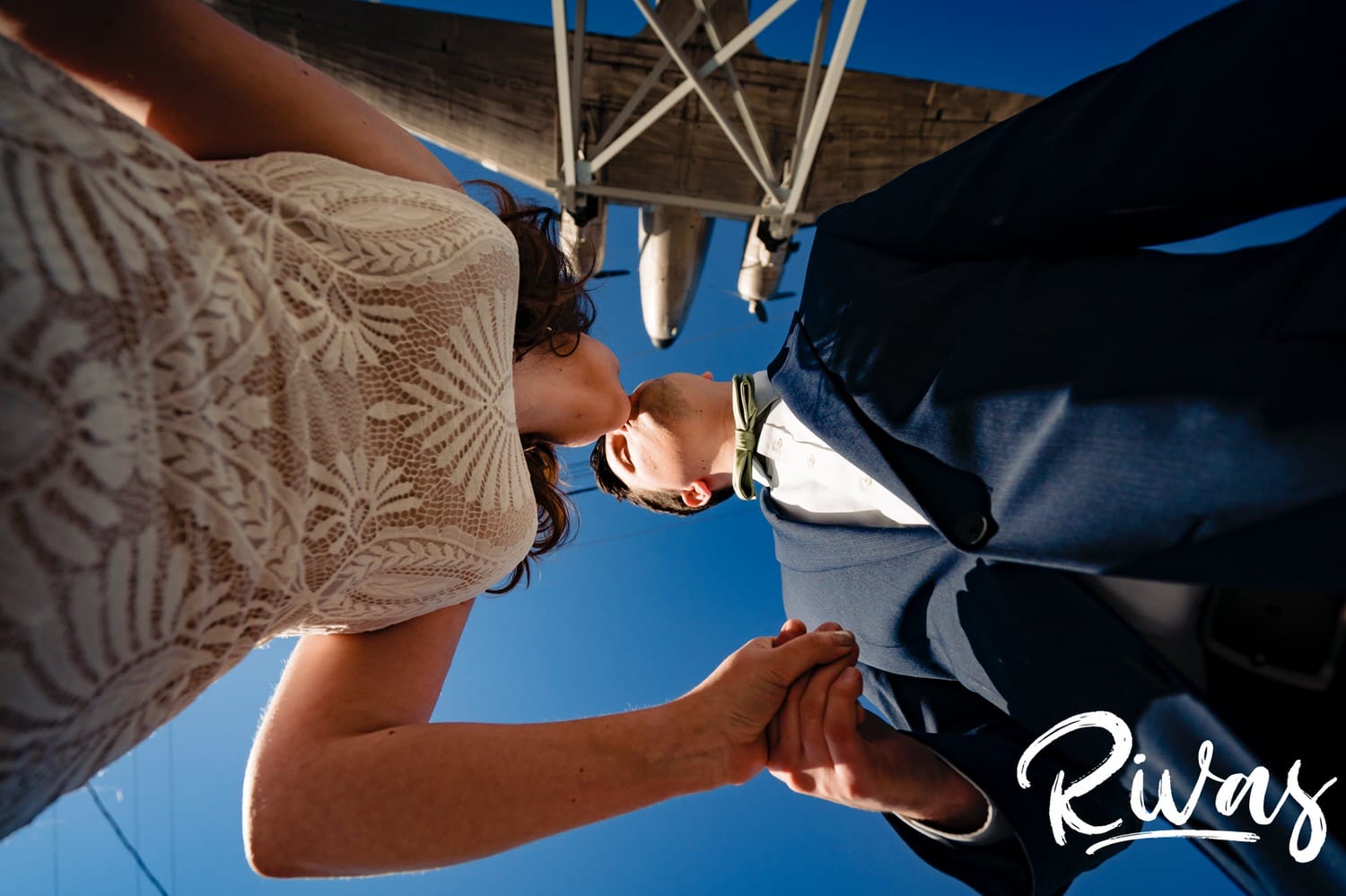 A colorful picture taken from the ground up of a bride and groom leaning in to share a kiss, the mounted Roasterie plane visible above them on their fall wedding day in Kansas city. 