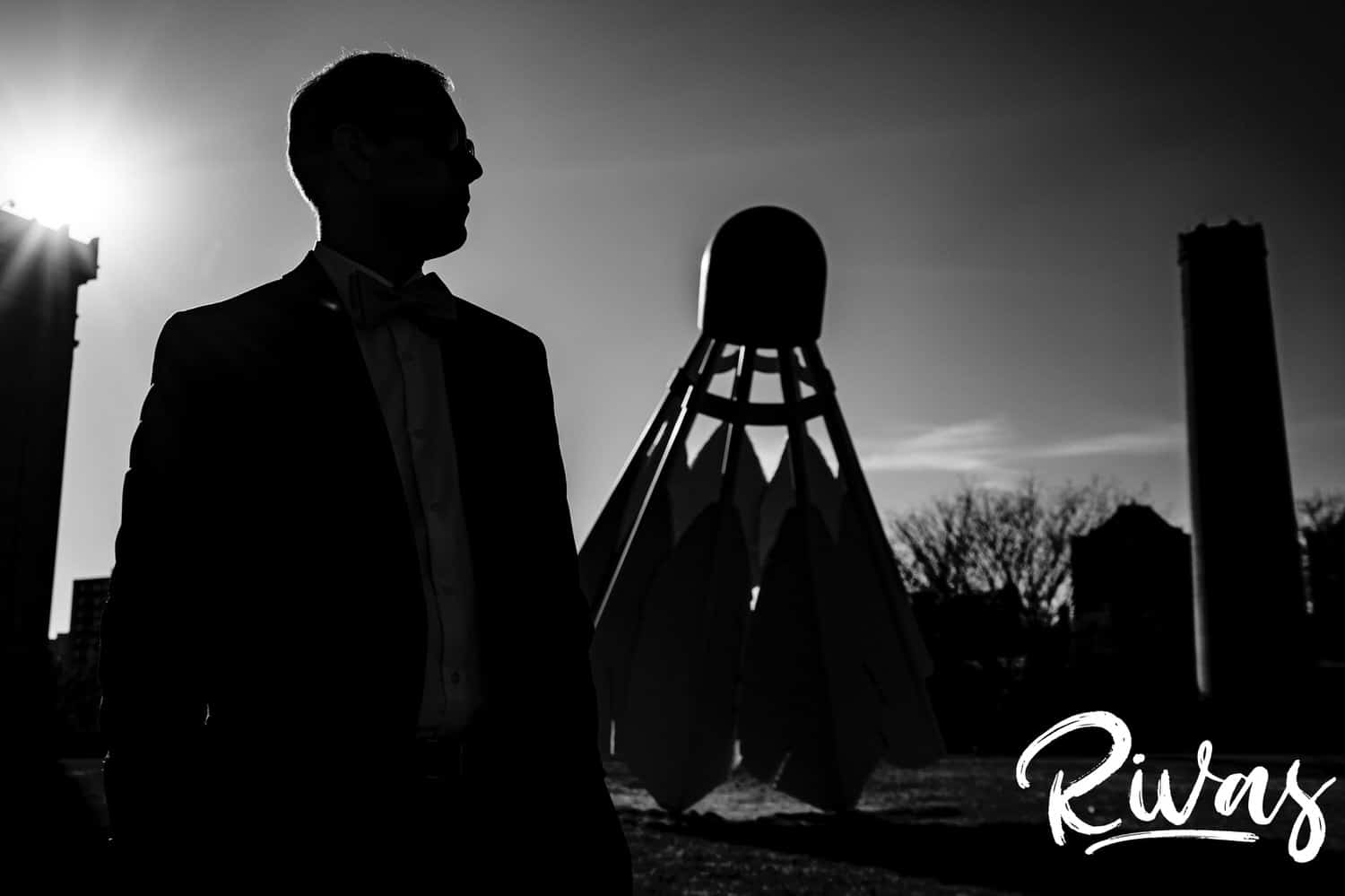 A bold black and white silhouette of a groomsmen looking off into the distance in front of a silhouetted shuttlecock on the back lawn of The Nelson Atkins Museum of Art on a fall wedding day in Kansas City. 