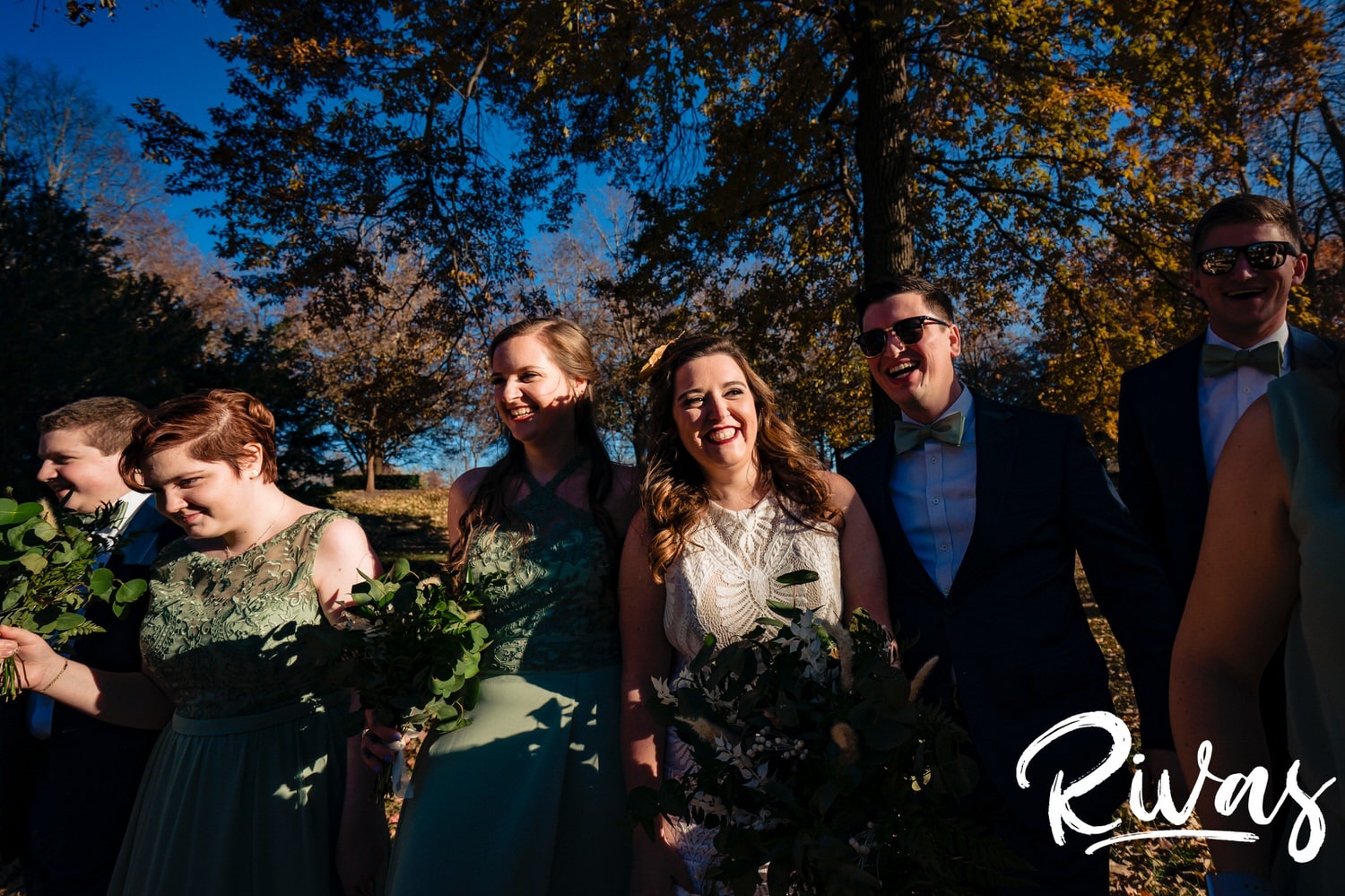 A colorful, candid picture of a bride and groom laughing with their wedding party on the lawn of The Nelson Atkins Museum of Art in Kansas City on their fall wedding day. 