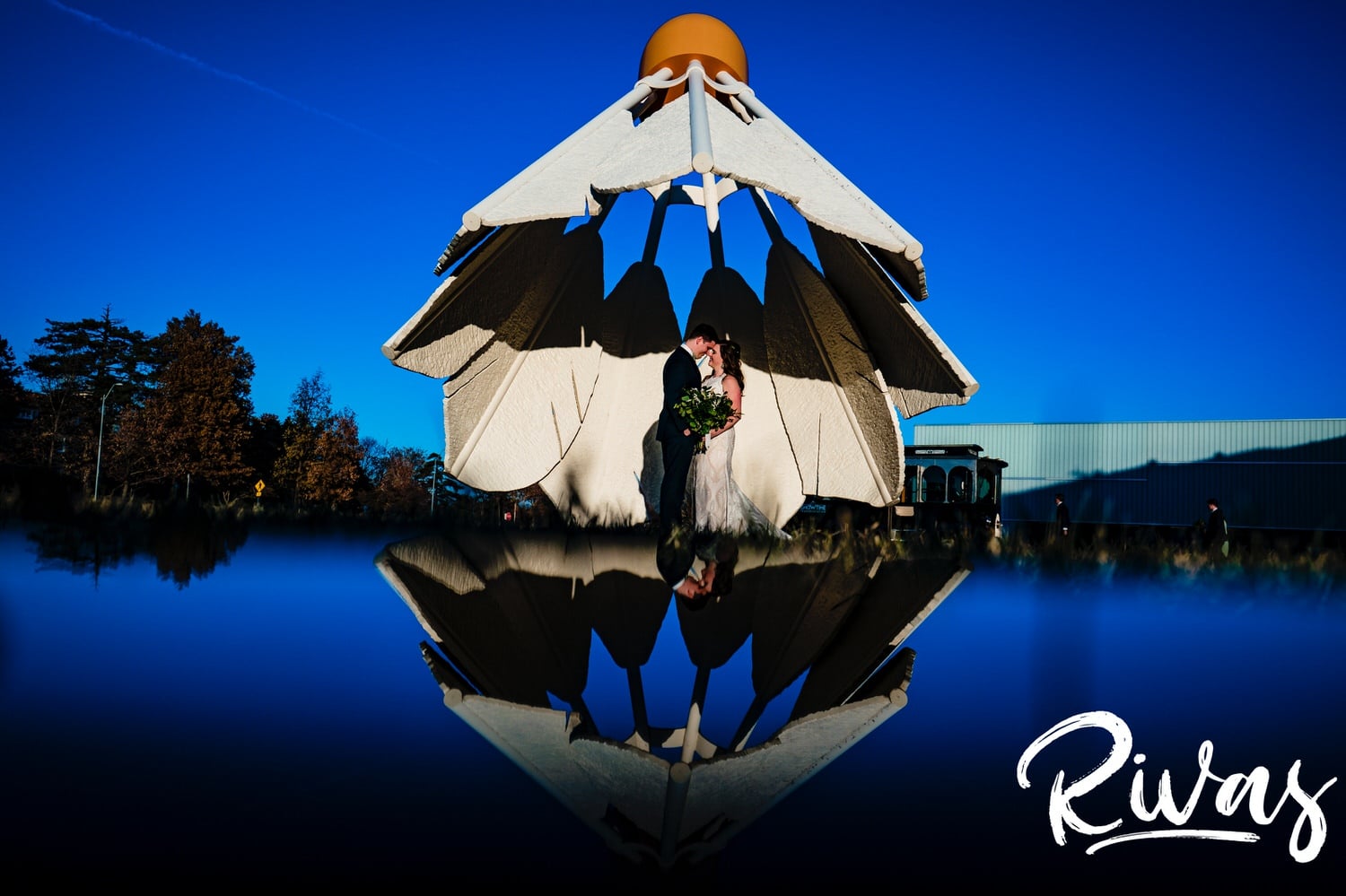 A colorful portrait of a bride and groom standing under a giant shuttlecock, reflected into the ground beneath them on their fall wedding day in Kansas City. 