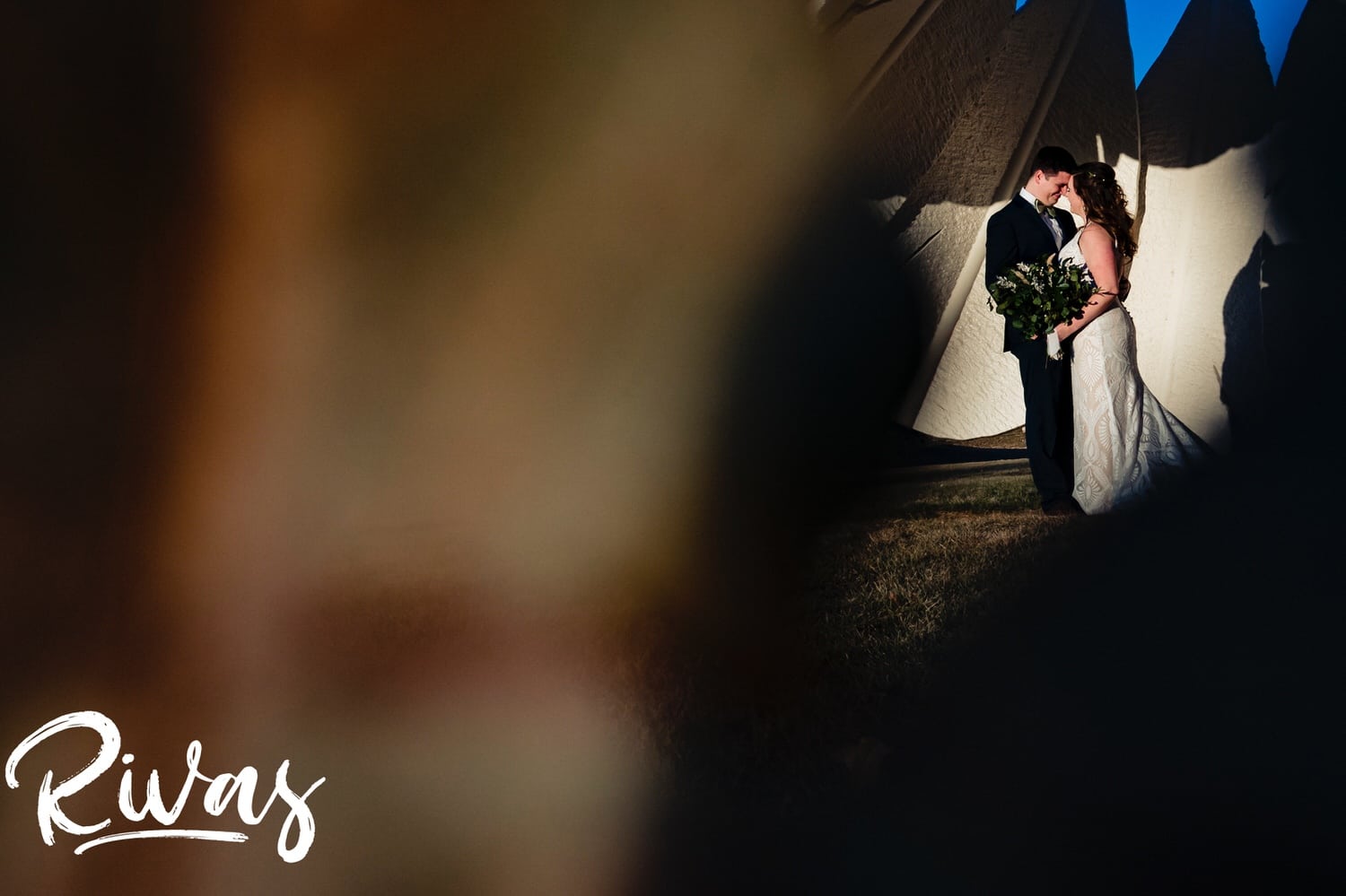 An intimate black and white picture taken through the cracks of a giant shuttlecock of a bride and groom sharing a kiss on the afternoon of their fall wedding day in Kansas City. 