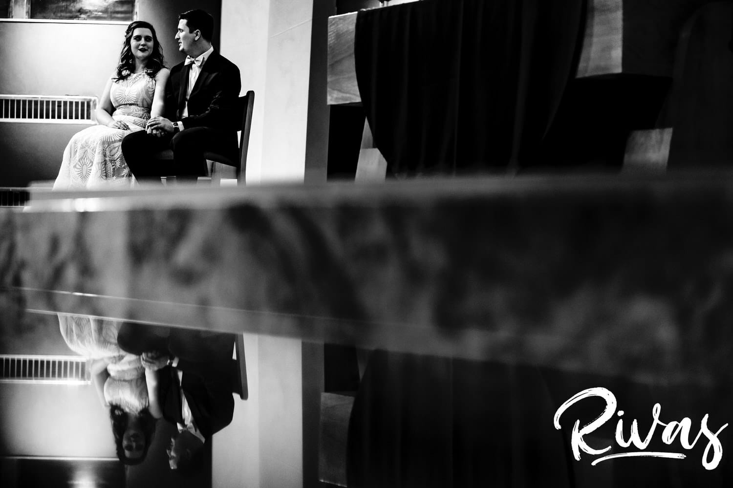 A candid black and white, reflected photo of a bride and groom sitting together during their Catholic wedding ceremony in Kansas City. 