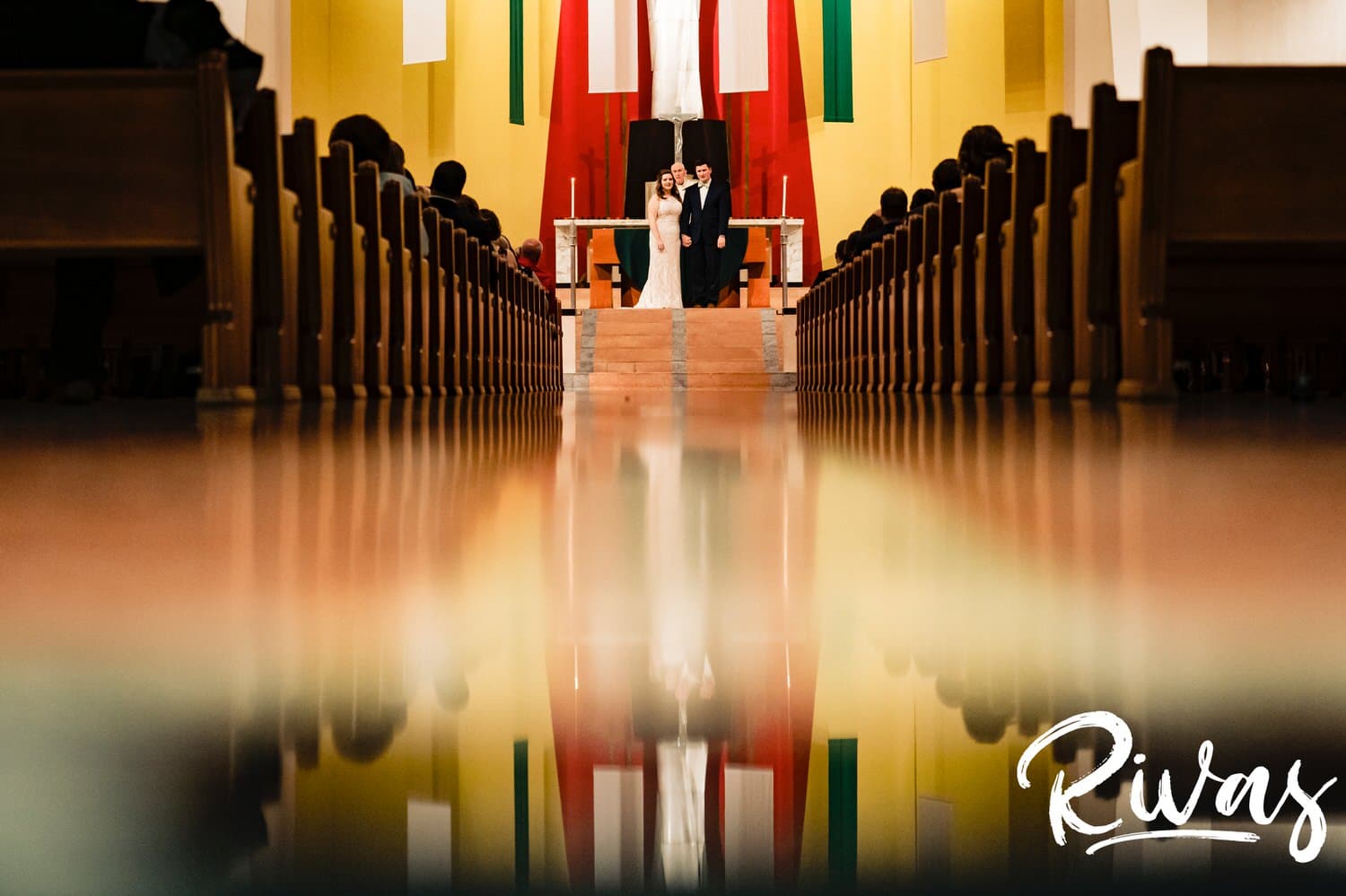 A colorful, reflective picture of a bride and groom holding hands, standing at the front of the church at the end of their wedding ceremony on a fall day in Kansas City. 