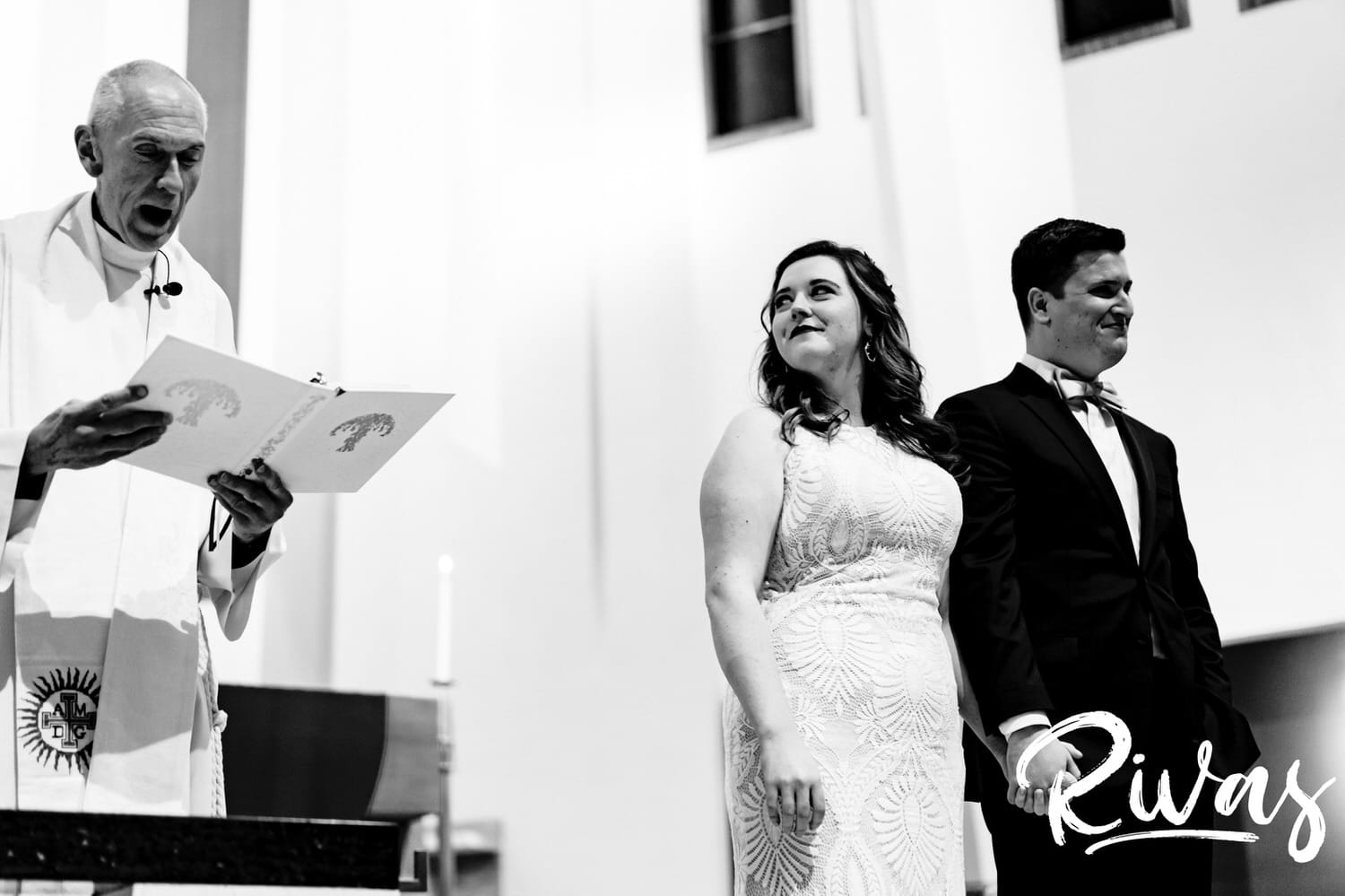 A black and white, reflective picture of a bride and groom holding hands, standing at the front of the church at the end of their wedding ceremony on a fall day in Kansas City. 