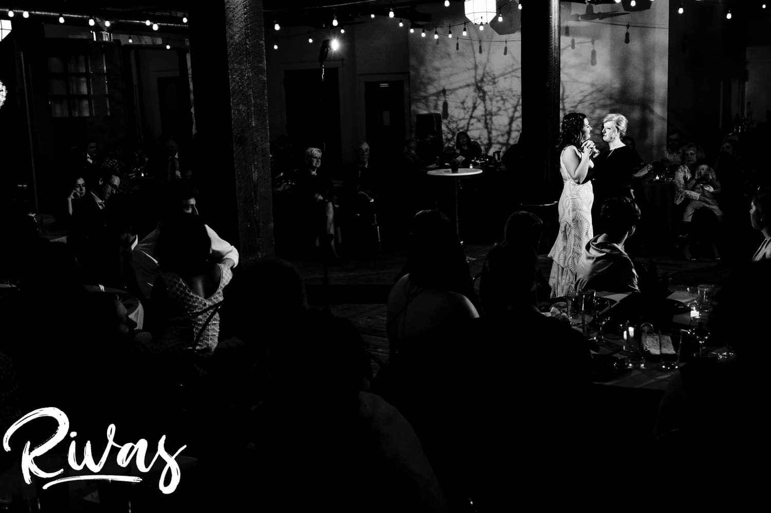 A candid black and white picture taken from across the room of a bride dancing with her mom during her wedding reception in Kansas City at The Foundation Event Space. 