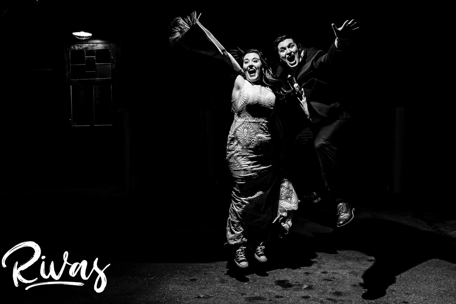 A candid black and white picture of a bride and groom enthusiastically jumping into the air in celebration at the end of their fall wedding reception in Kansas City. 