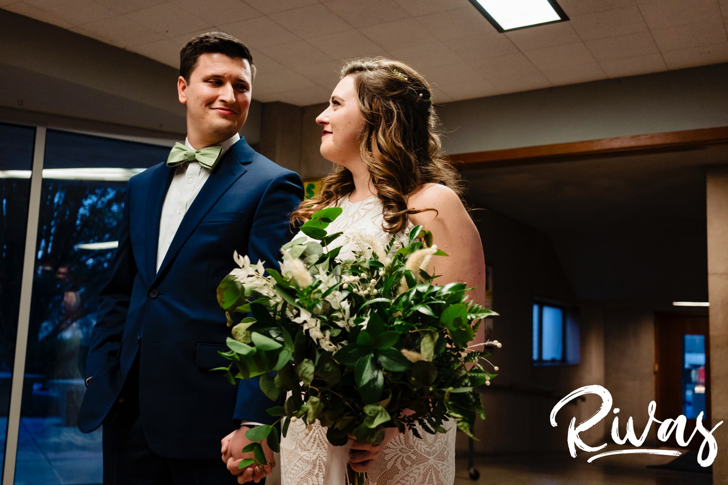 A colorful, candid picture of a bride and groom holding hands and looking at each other second before they walk down the aisle to their wedding ceremony together on their fall wedding day in Kansas City. 