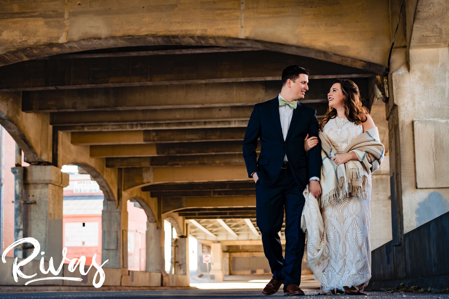 A colorful, candid picture of a bride and groom walking arm in arm up the 12th Street viaduct Bridge in Kansas City on the afternoon of their fall wedding day. 