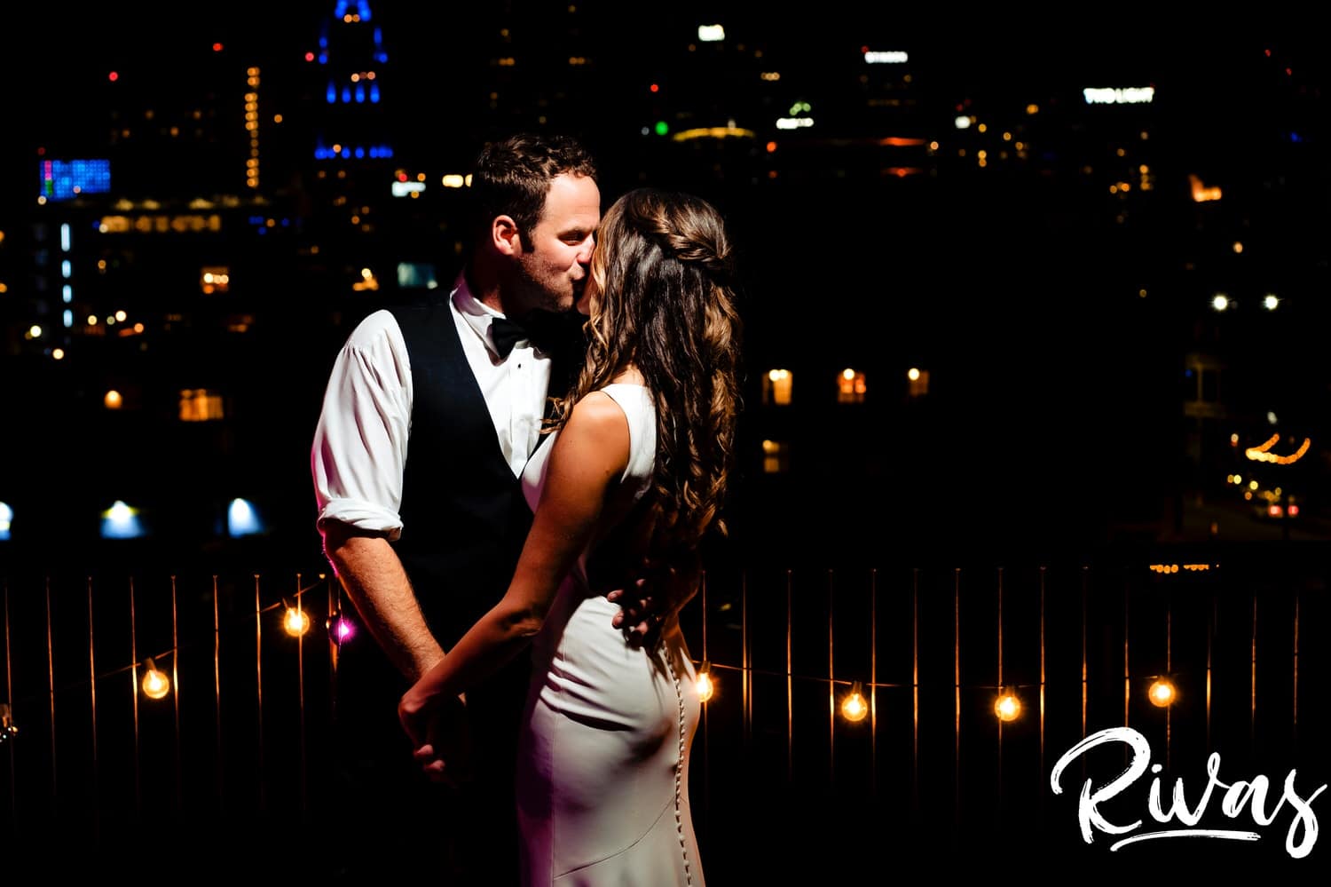 A dramatic, romantic end-of-the-night photo of a bride and groom holding hands and sharing a kiss at the end of their KC Skyline wedding day. 