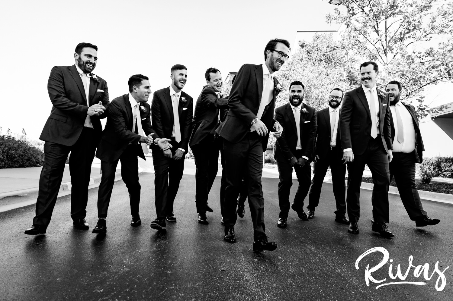 A bold black and white, candid picture of a groom and his groomsmen walking down the street laughing on the afternoon of a wedding reception at The Museum at Prairiefire in Kansas City. 