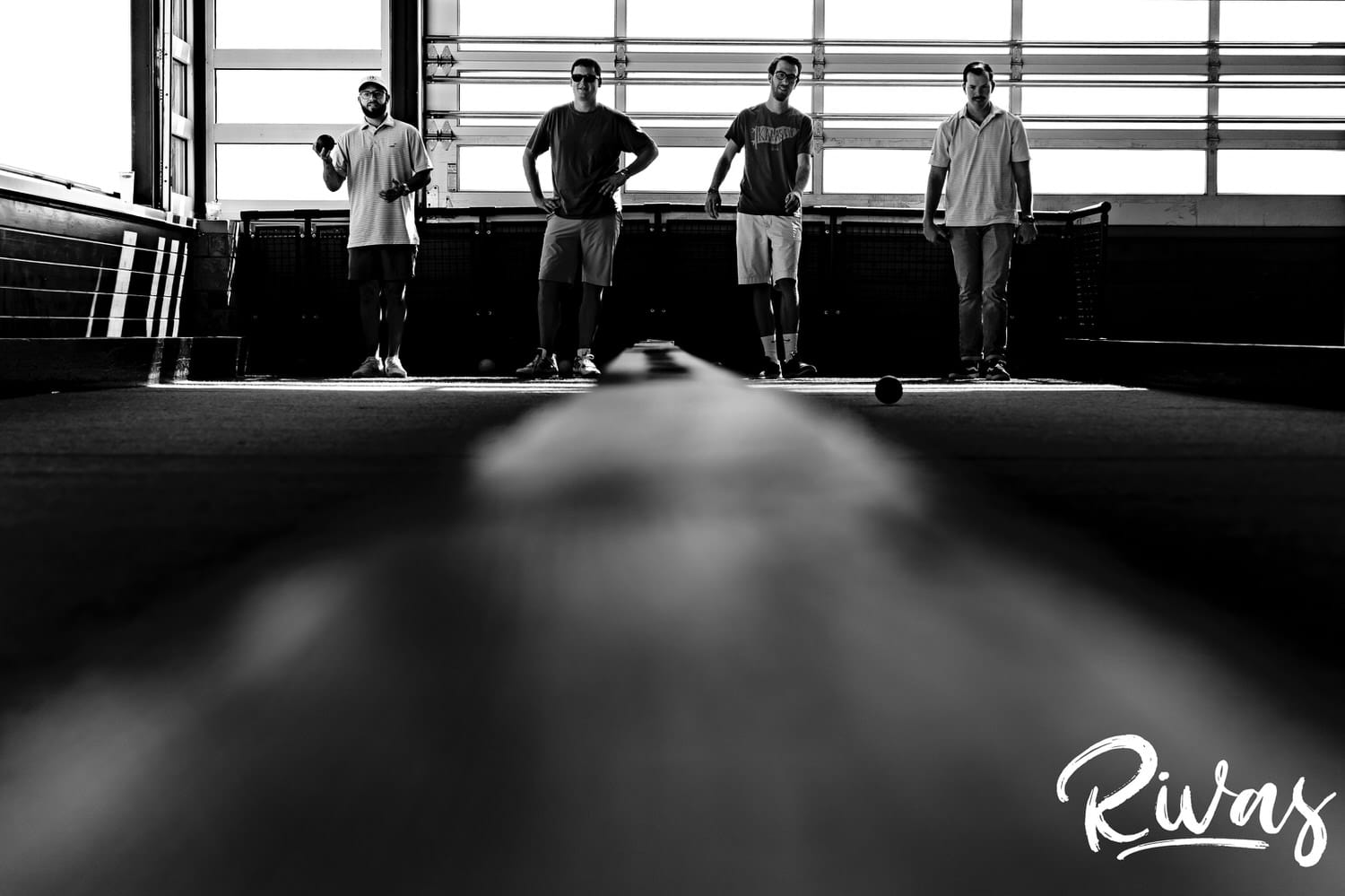 A black and white picture taken from the end of a bocce ball court of a groom and his groomsmen getting ready to plan on the morning of his Museum at Prairiefire Wedding Reception day in Kansas City. 
