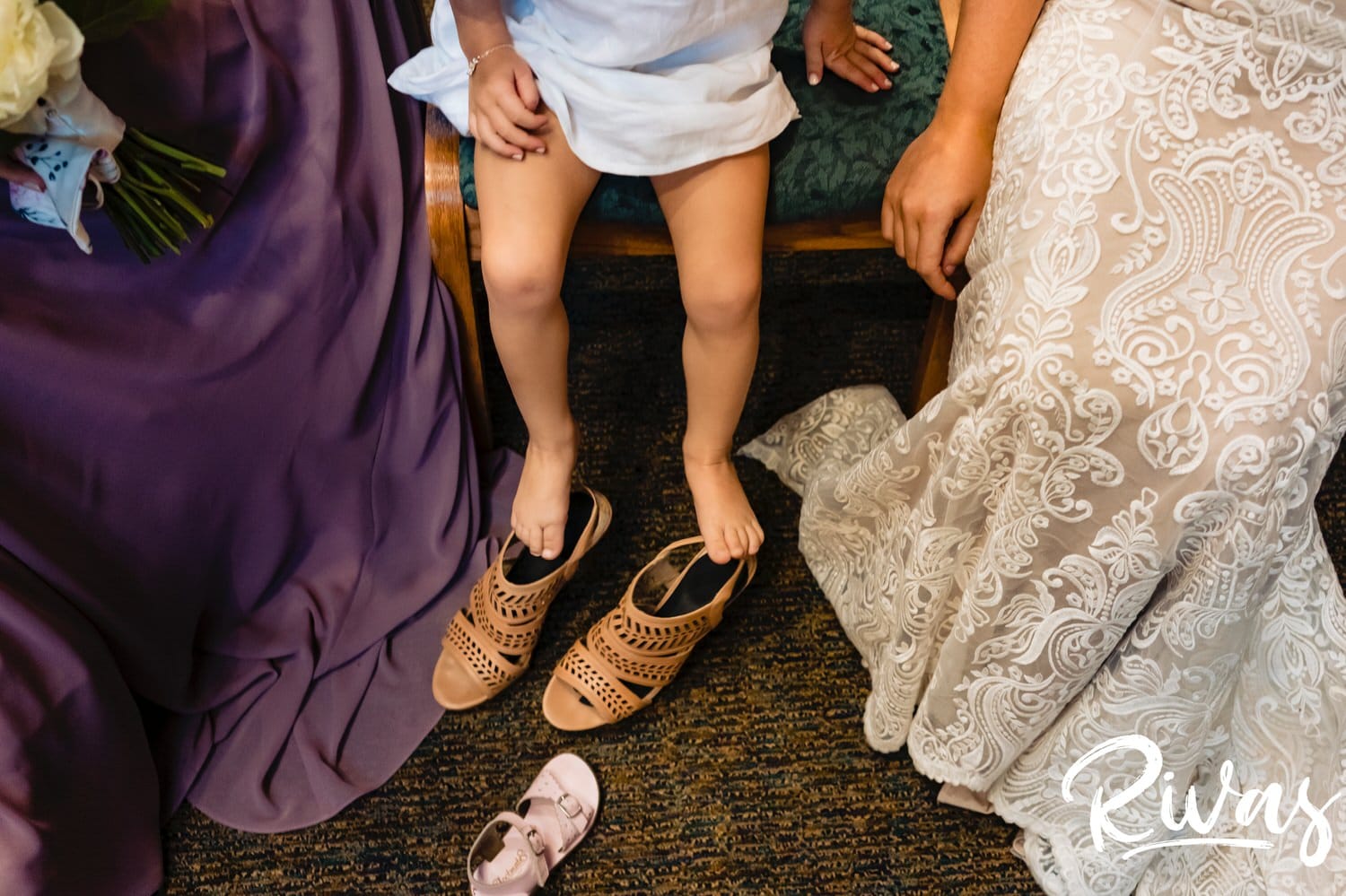A colorful, candid picture of a tiny flowergirl attempting to put on the bride's high heels on the afternoon of a wedding in Overland Park. 