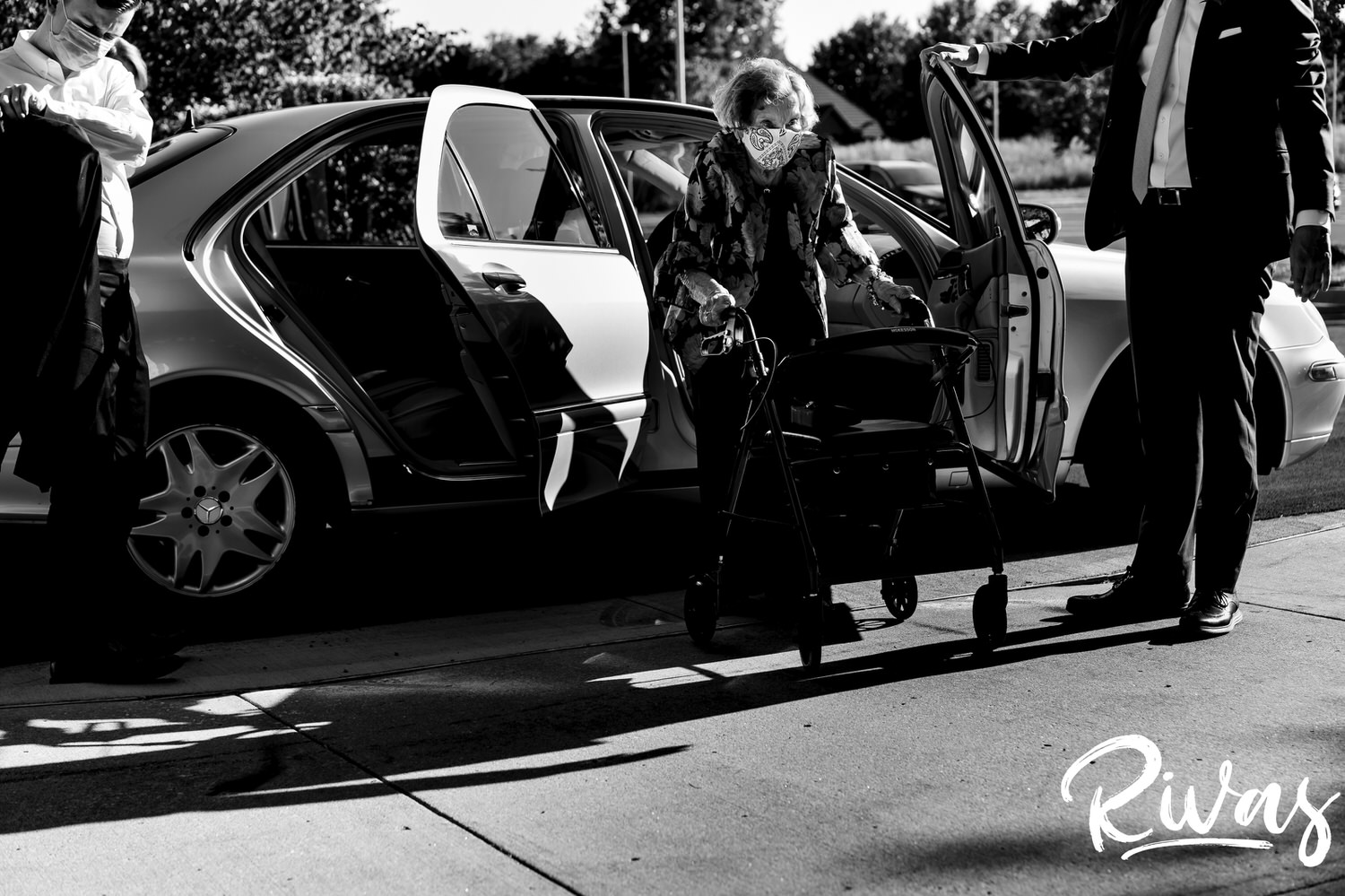 A candid black and white picture of a groom's grandma stepping out of a car with a mask on to attend a wedding ceremony in Overland Park. 