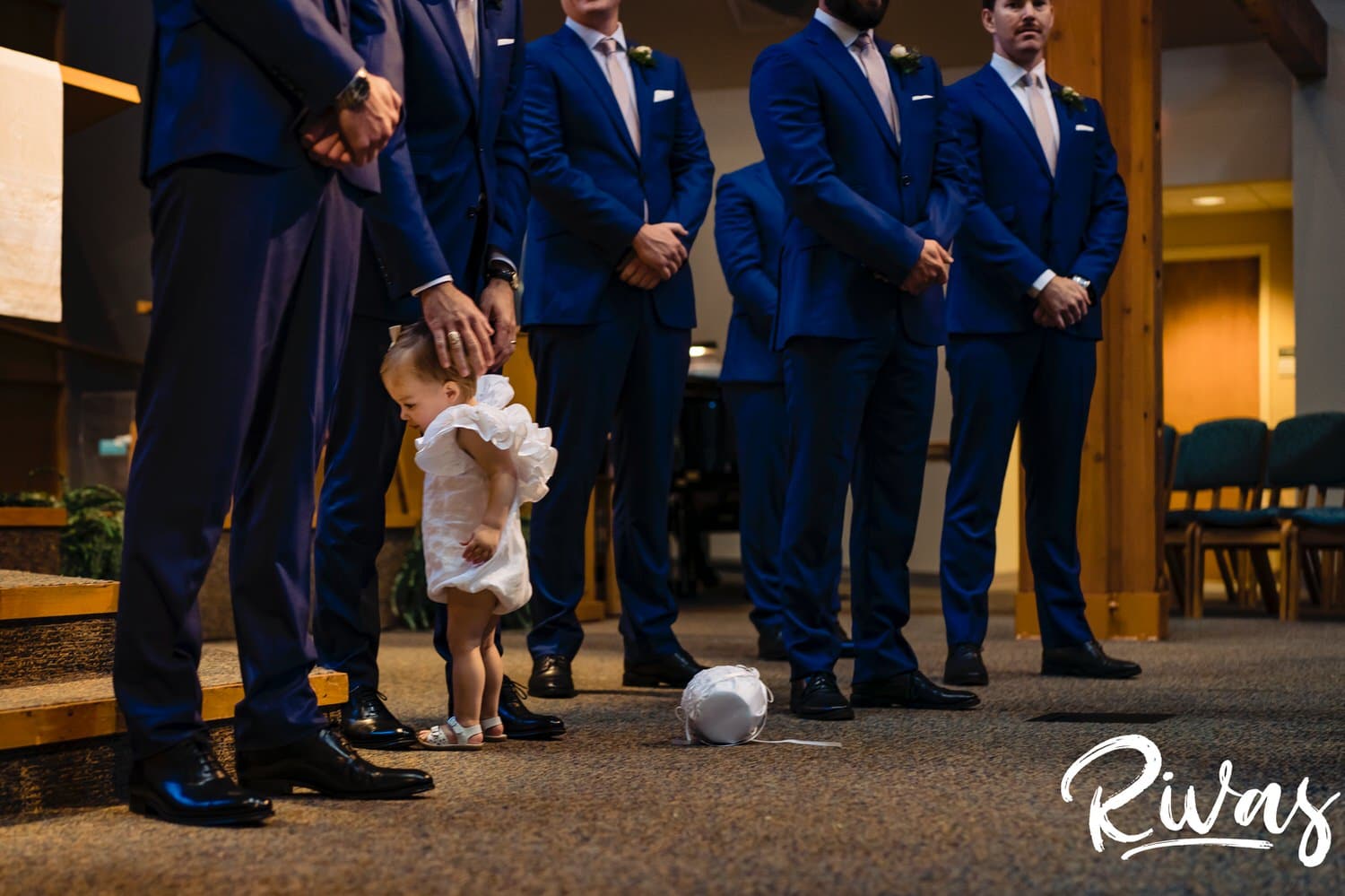 A colorful, candid picture of a flowergirl hugging her dad's legs during a wedding ceremony in Overland Park. 