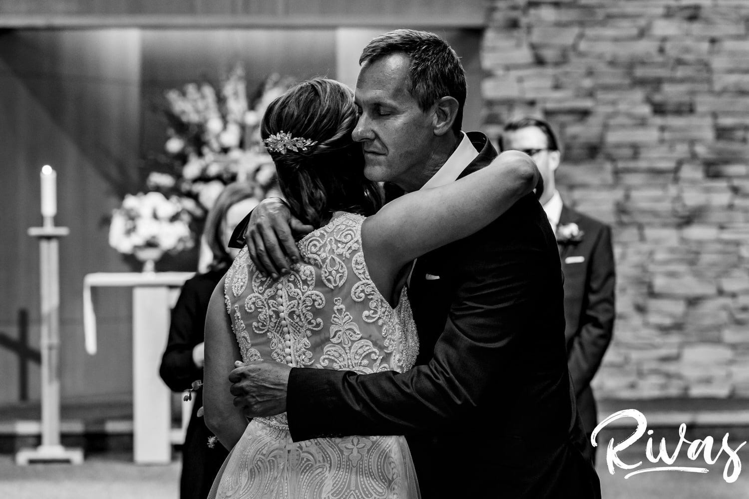 A candid black and white picture of a bride's dad emotionally hugging his daughter as he gives her away during her wedding ceremony. 