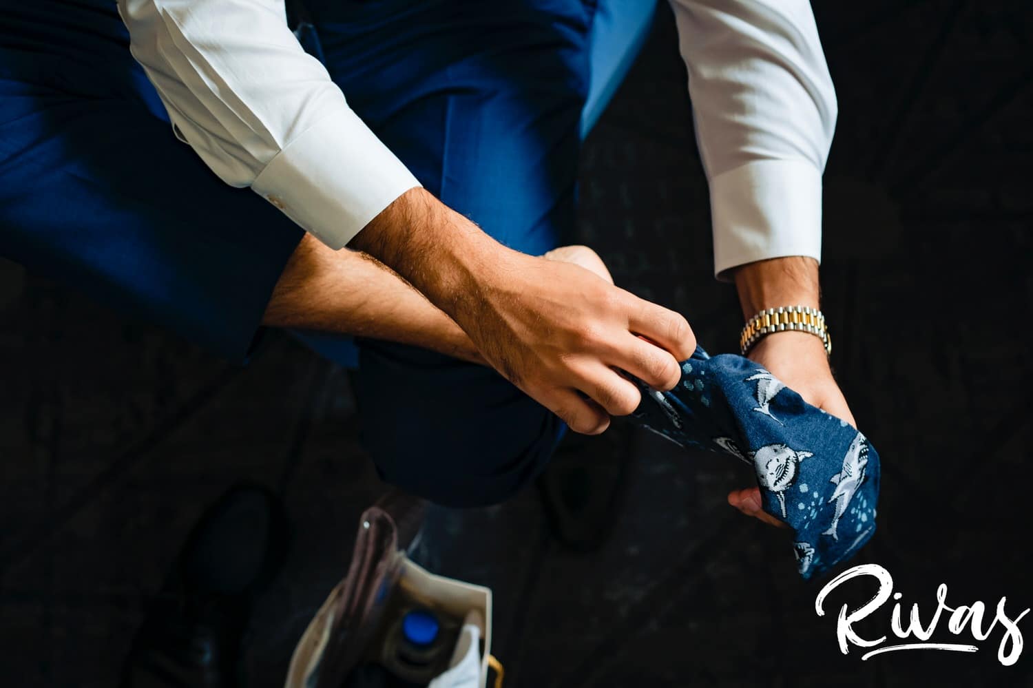 A detailed picture of a man in a blue suit pulling on a pair of navy blue shark socks as he gets dressed on a wedding morning in Leawood. 