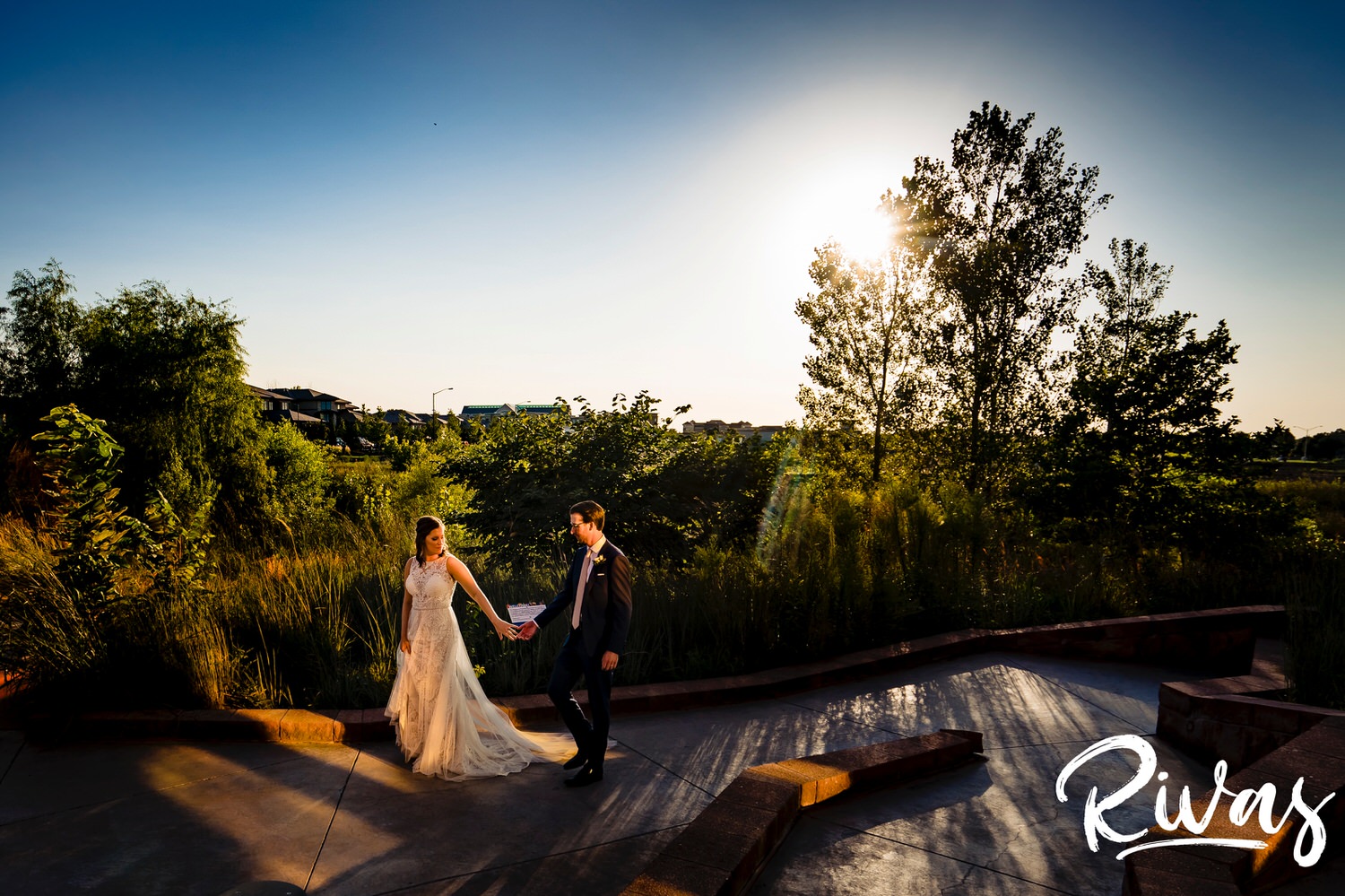 A wide, candid picture of a bride and groom walking hand-in-hand across the back patio of The Museum at Prairiefire on their wedding day. 