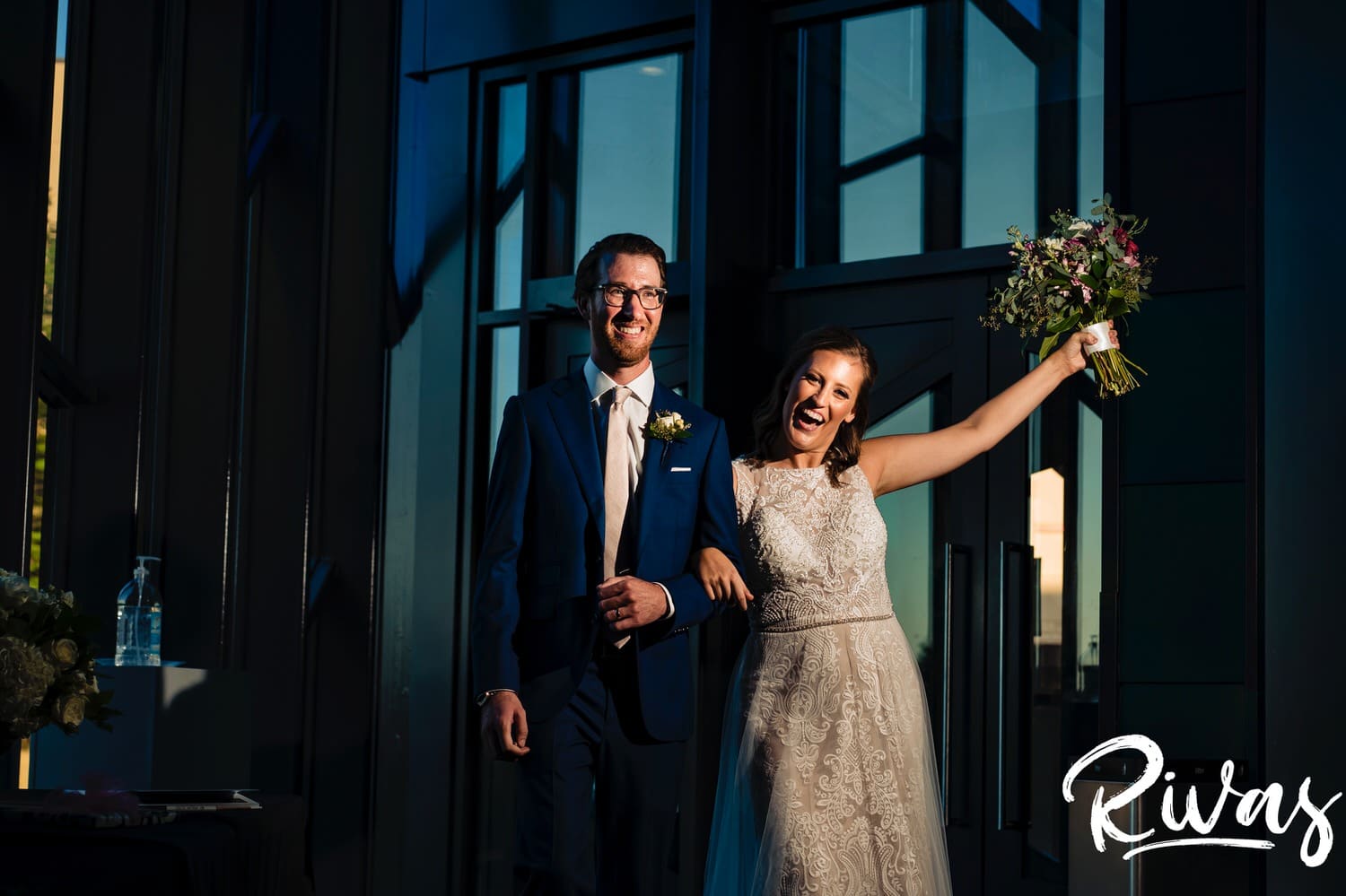 A colorful picture of a bride and groom with their arms in the air in celebration walking into their Museum at Prairiefire wedding reception. 