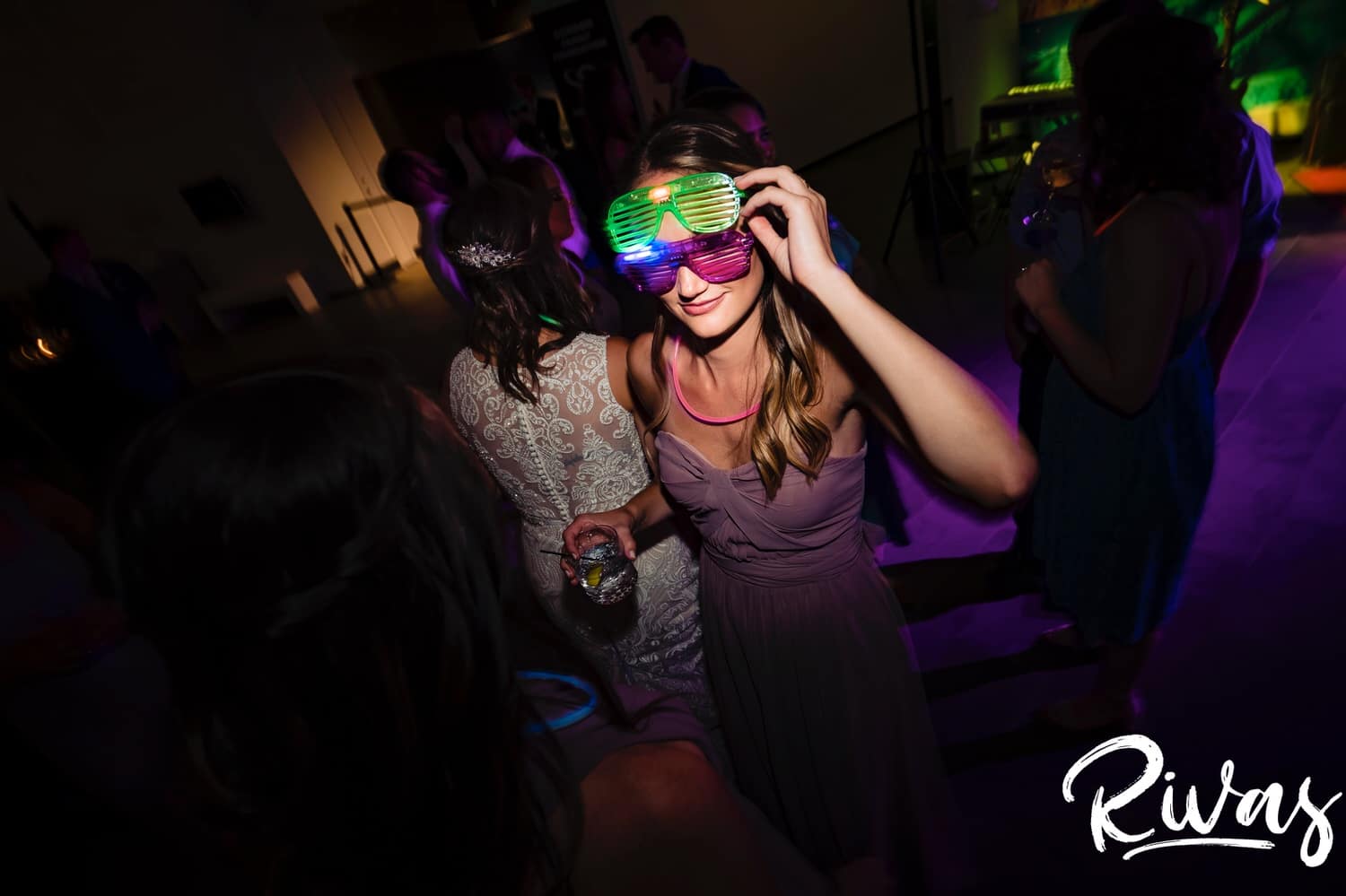 A colorful, candid picture of a bridesmaid with light up glasses on dancing her way across the dancefloor at a Museum at Prairiefire wedding reception. 