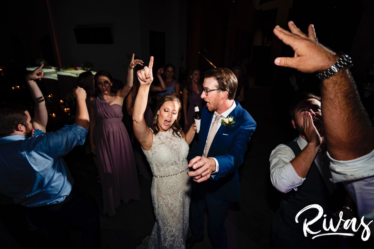 A candid picture of a bride and groom, arms up in the air dancing during their Museum at Prairiefire wedding reception. 