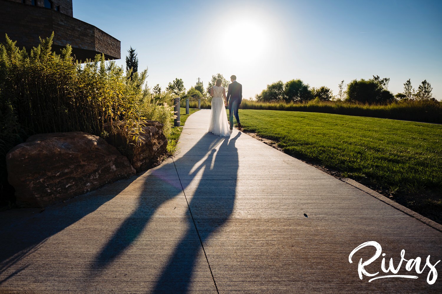 A colorful picture of a bride and groom holding hands and walking off into the sunset on the day of their wedding reception at The Museum at Prairiefire in Leawood. 