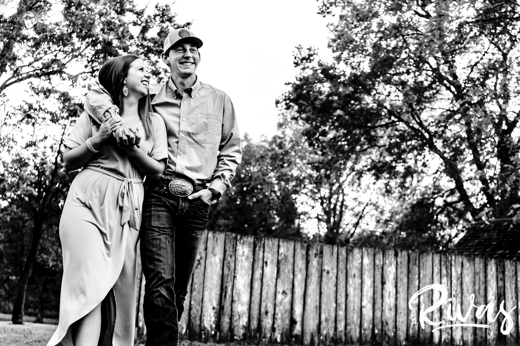 A candid black and white picture of an engaged couple, the mans' arm casually draped around the woman's shoulders as she smiles and looks up at him during their rustic fall engagement session in Kansas City. 