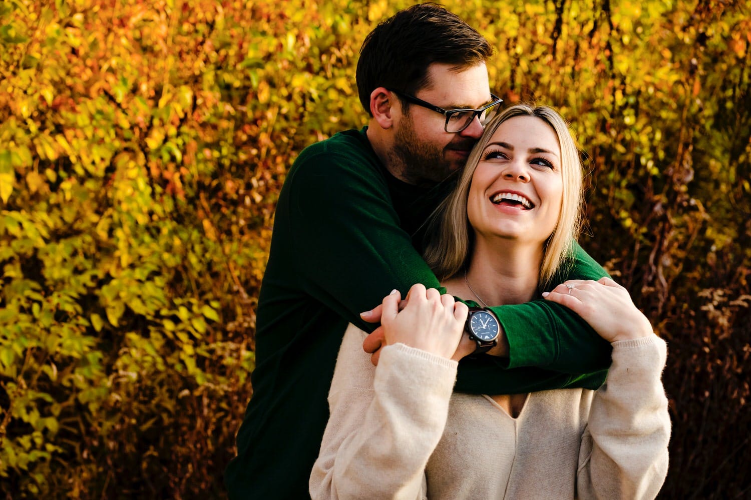 A colorful, close-up picture of an engaged couple, the mans arms wrapped around the woman's shoulders as he leans in to give her a kiss during their SMP fall engagement session in Kansas city. 