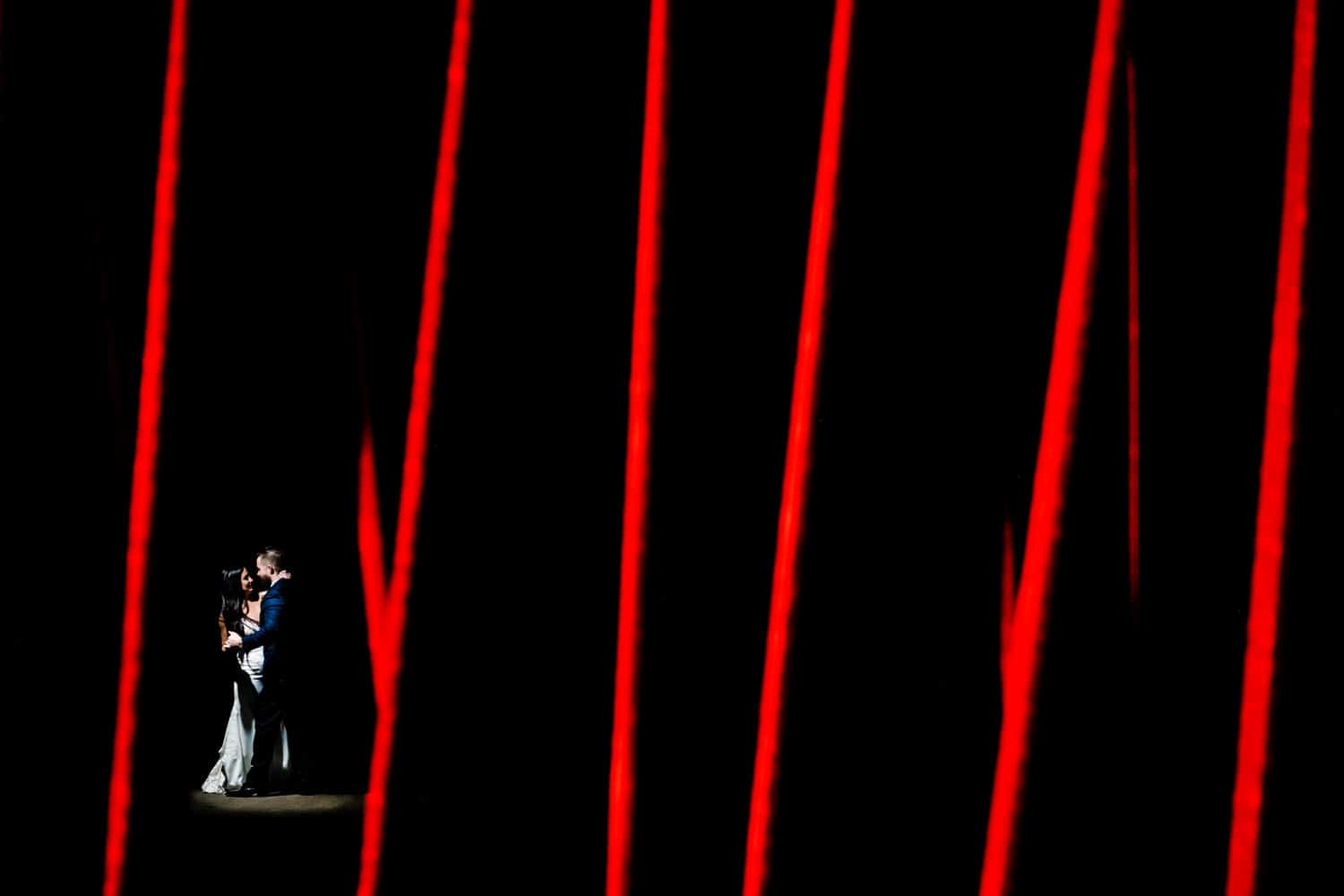 A bold portrait of a bride and groom dancing behind a set of red criss-crossed bars on the day of their 2020 KC wedding. 