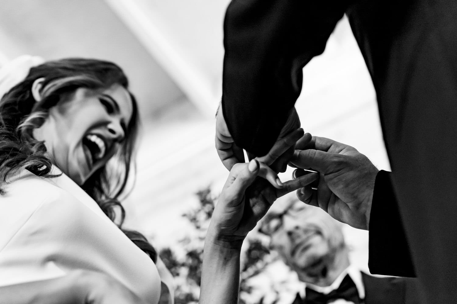 A candid black and white picture taken from the ground looking up of a groom putting a ring on a bride's hand during their 2020 KC wedding ceremony at The Otten on Main. 