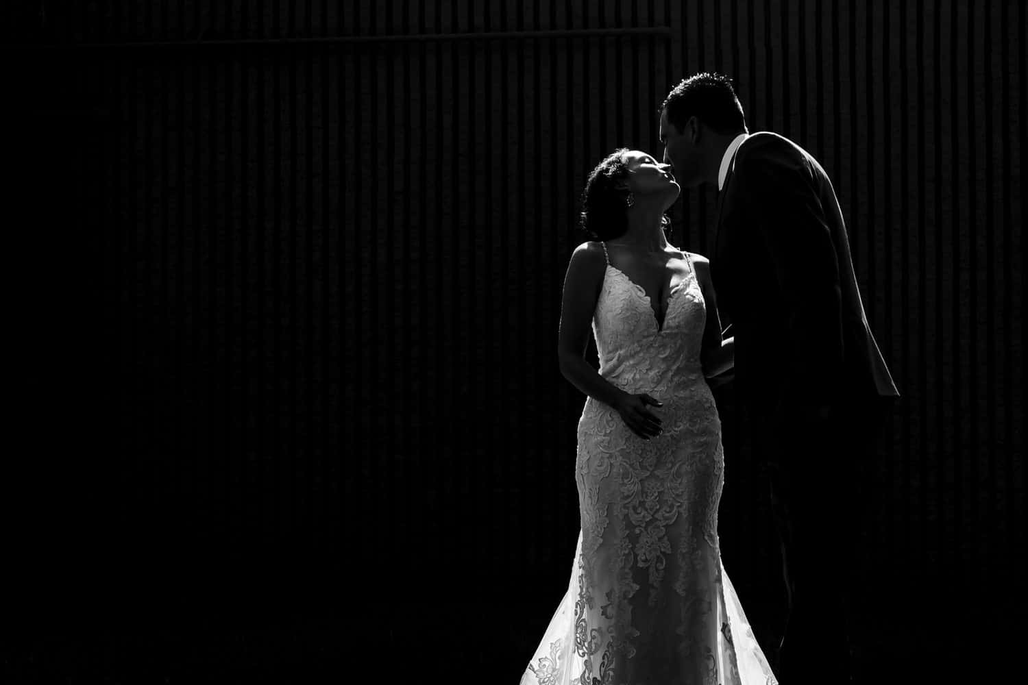 A dramatic black and white portrait of a groom leaning in to kiss his bride on the day of their 2020 wedding in Kansas City. 