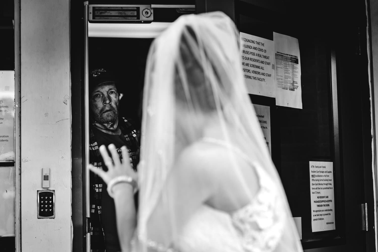 A candid black and white picture of a bride waving at her dad, in the hospital, on the day of her 2020 wedding in Kansas City. 