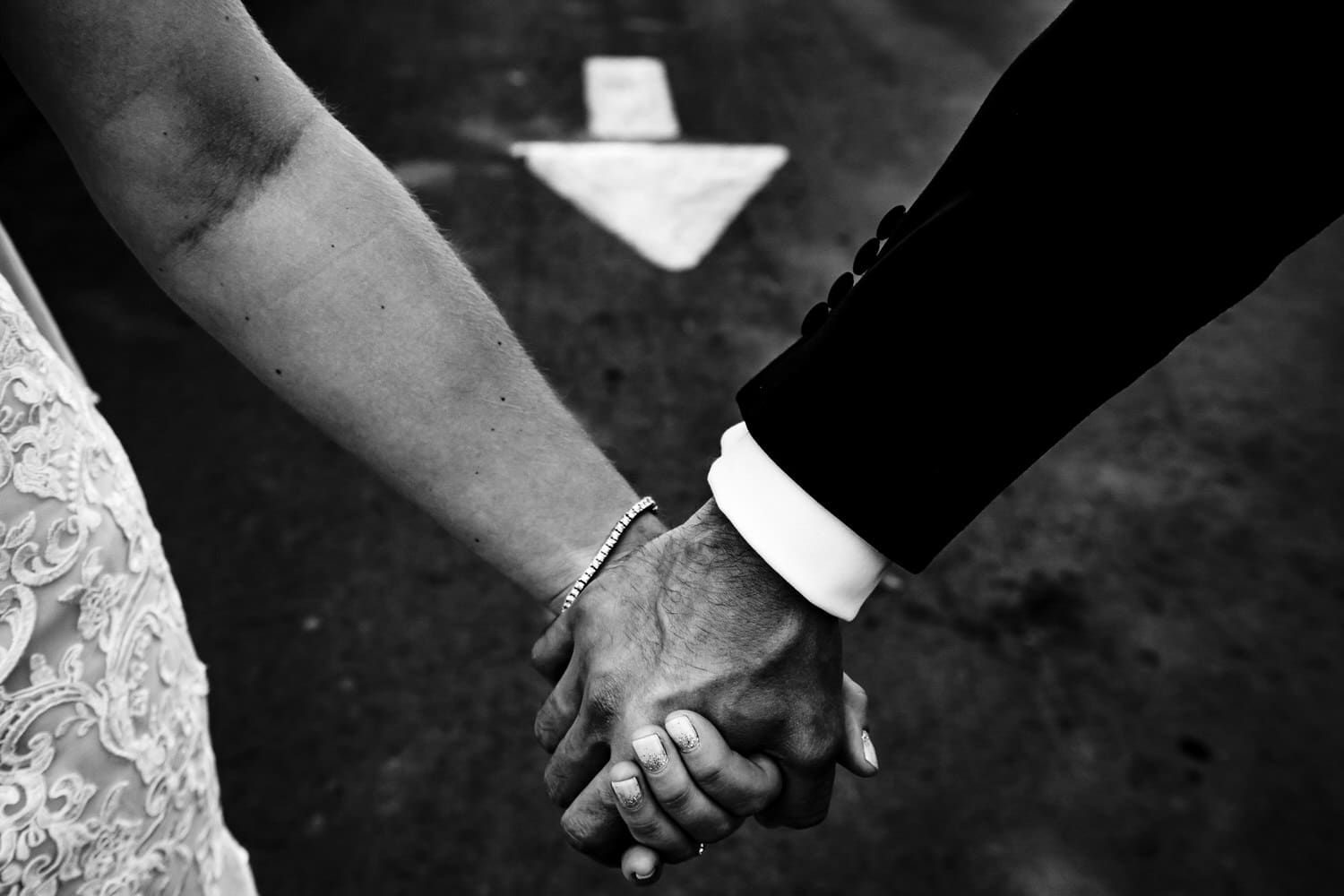 A candid black and white picture of a bride and groom holding hands, an arrow on the ground pointing at their hands on the day of their 2020 KC wedding. 