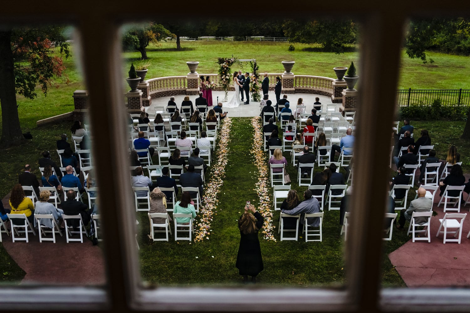 A colorful picture taken through a window of a weedding ceremony taking place on the lawn of Longview Mansion in Kansas City. 